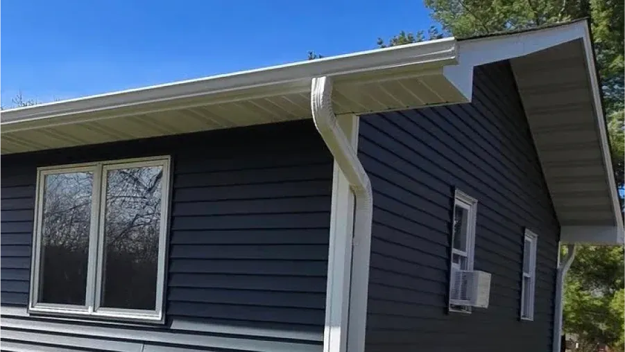 Dark blue house with white trim, gutters, and windows against a blue sky.
