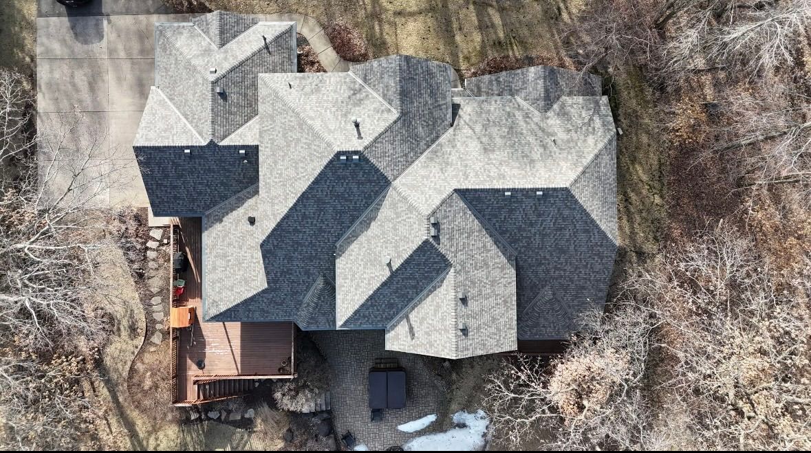 Exterior view of a house with brown siding, tan brick, and a deck against a blue sky.