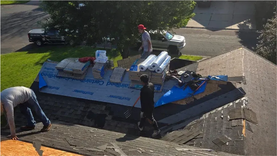 Roofers working on a house roof, surrounded by supplies, on a sunny day.