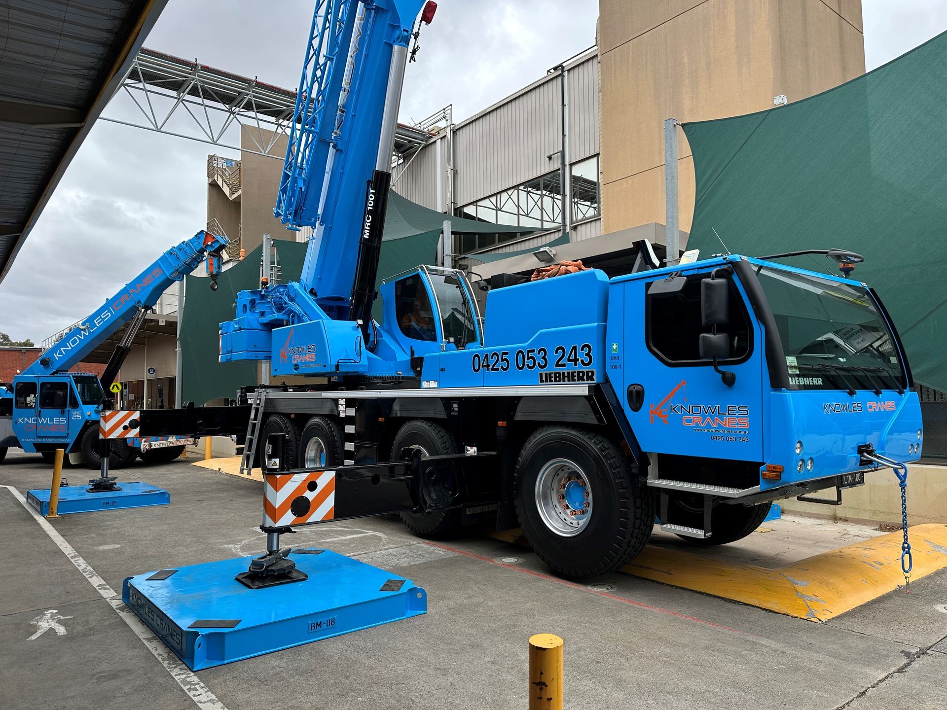 A blue truck with a crane on top of it is parked in a parking lot.