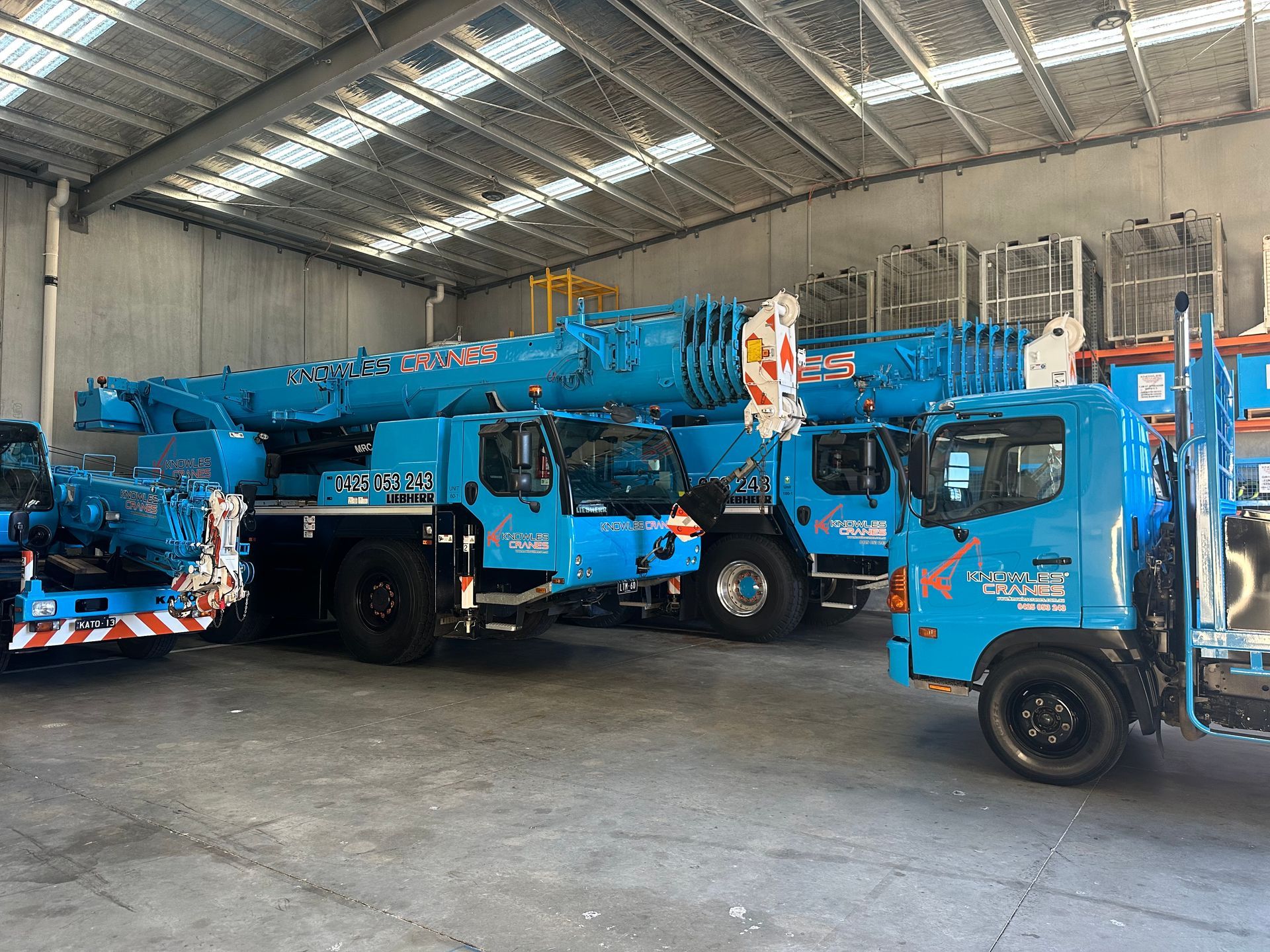 Fleet of Knowles Cranes vehicles parked inside warehouse, including cranes and support truck.