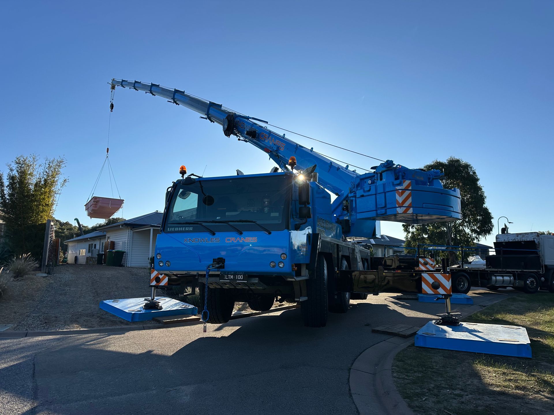 Liebherr crane lifting a pink fibreglass pool into a residential property at sunset.