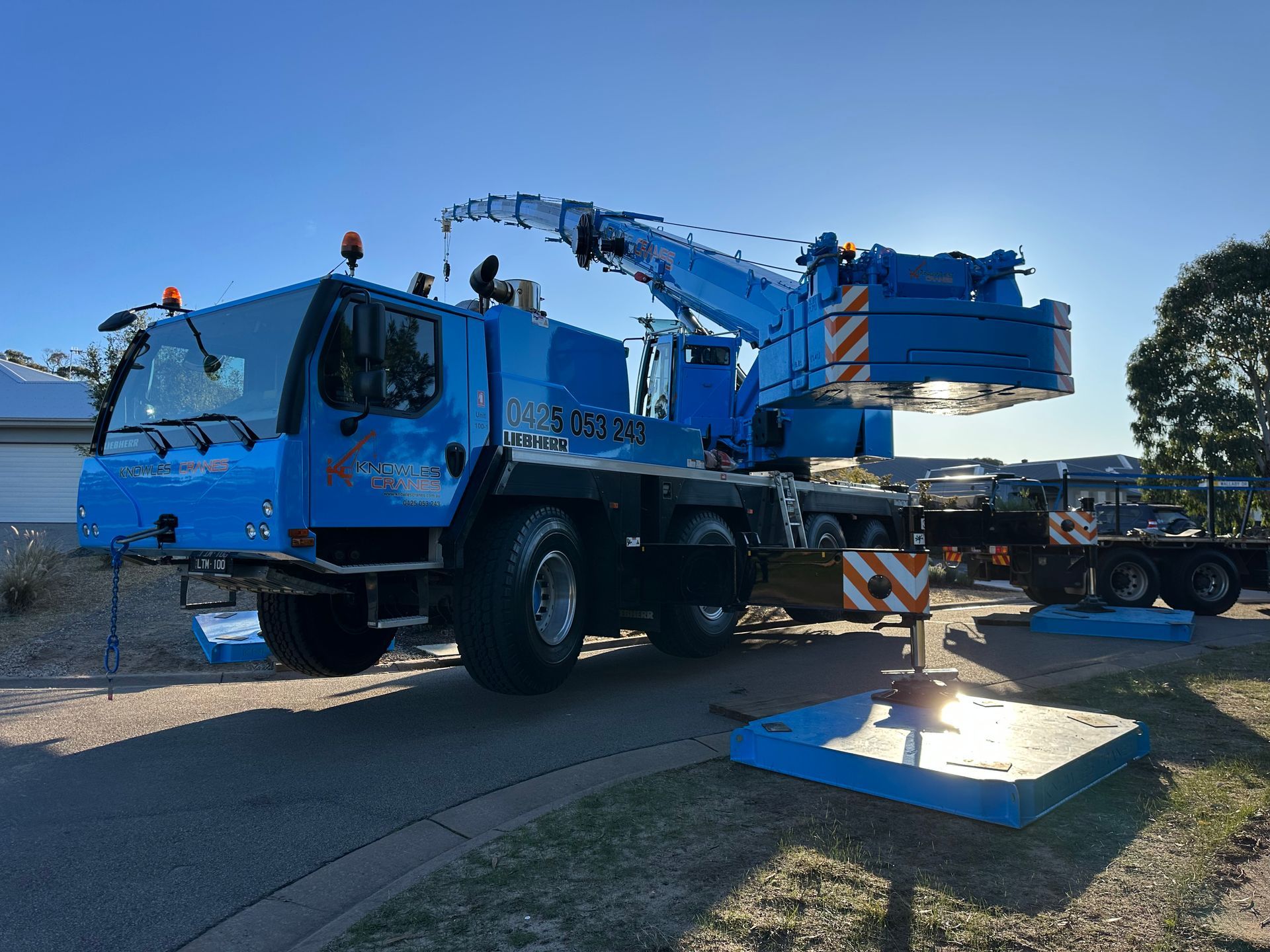 A Liebherr crane from Knowles Cranes lifting equipment at a residential site during daytime operation.