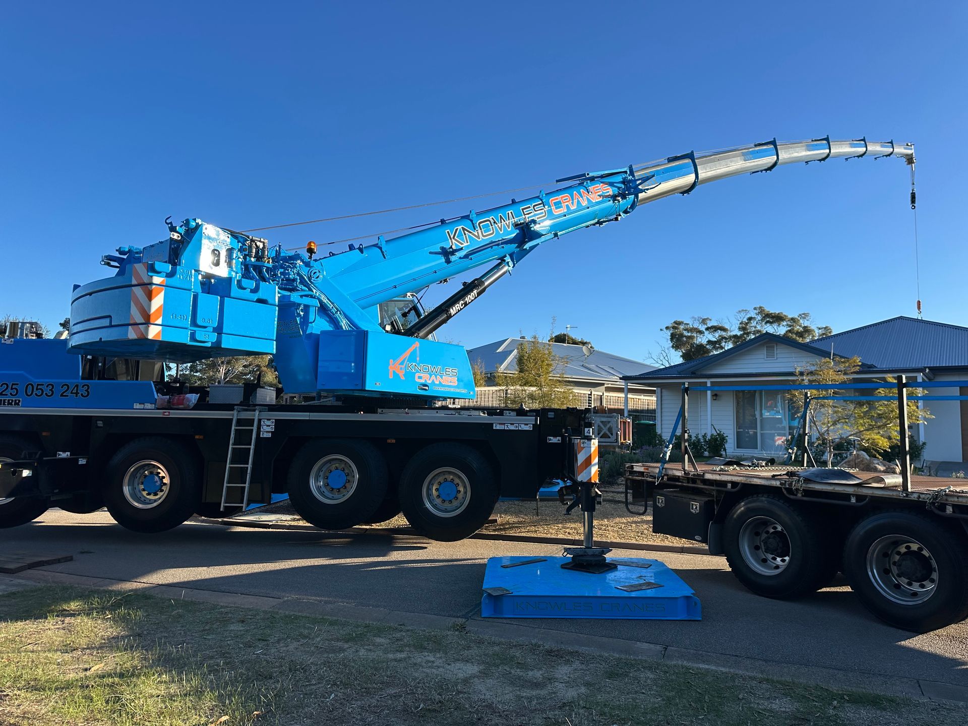 A blue truck with a crane attached to it is parked in front of a house.
