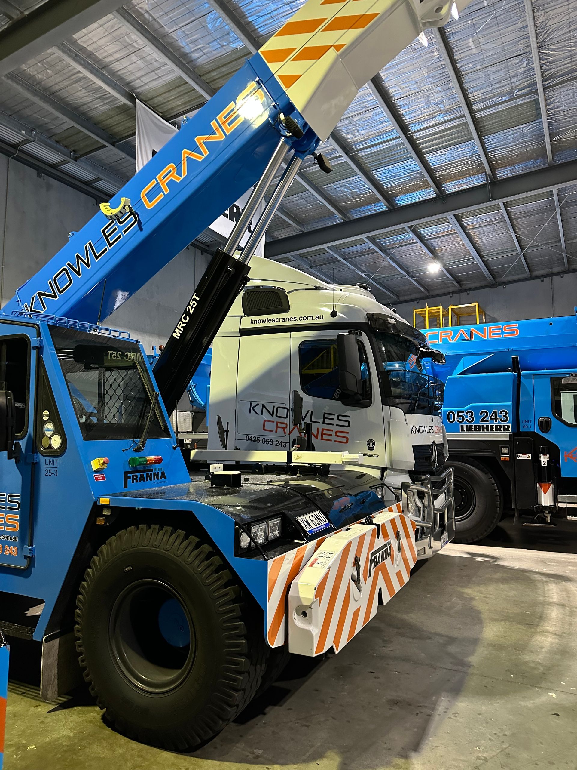 Close-up of Knowles Cranes Franna MAC 25 crane beside a branded transport truck inside an industrial shed.