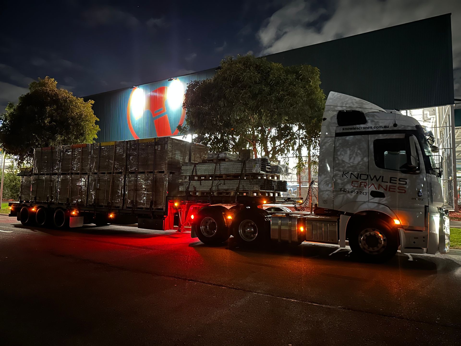 Knowles Cranes transport truck loaded with equipment and parked at night under illuminated signage.