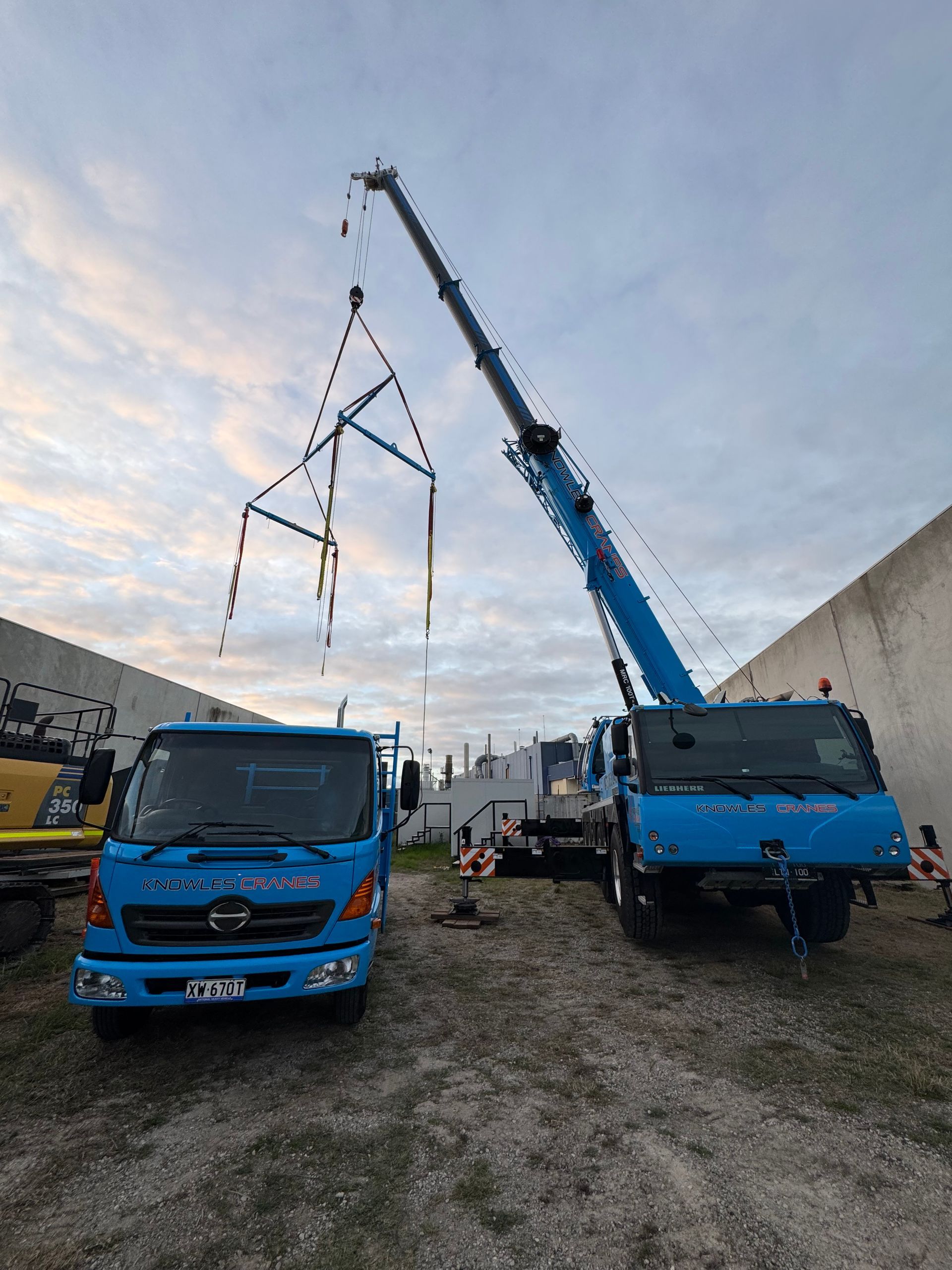 Mobile crane lifting custom rig at tight-access industrial site at sunset
