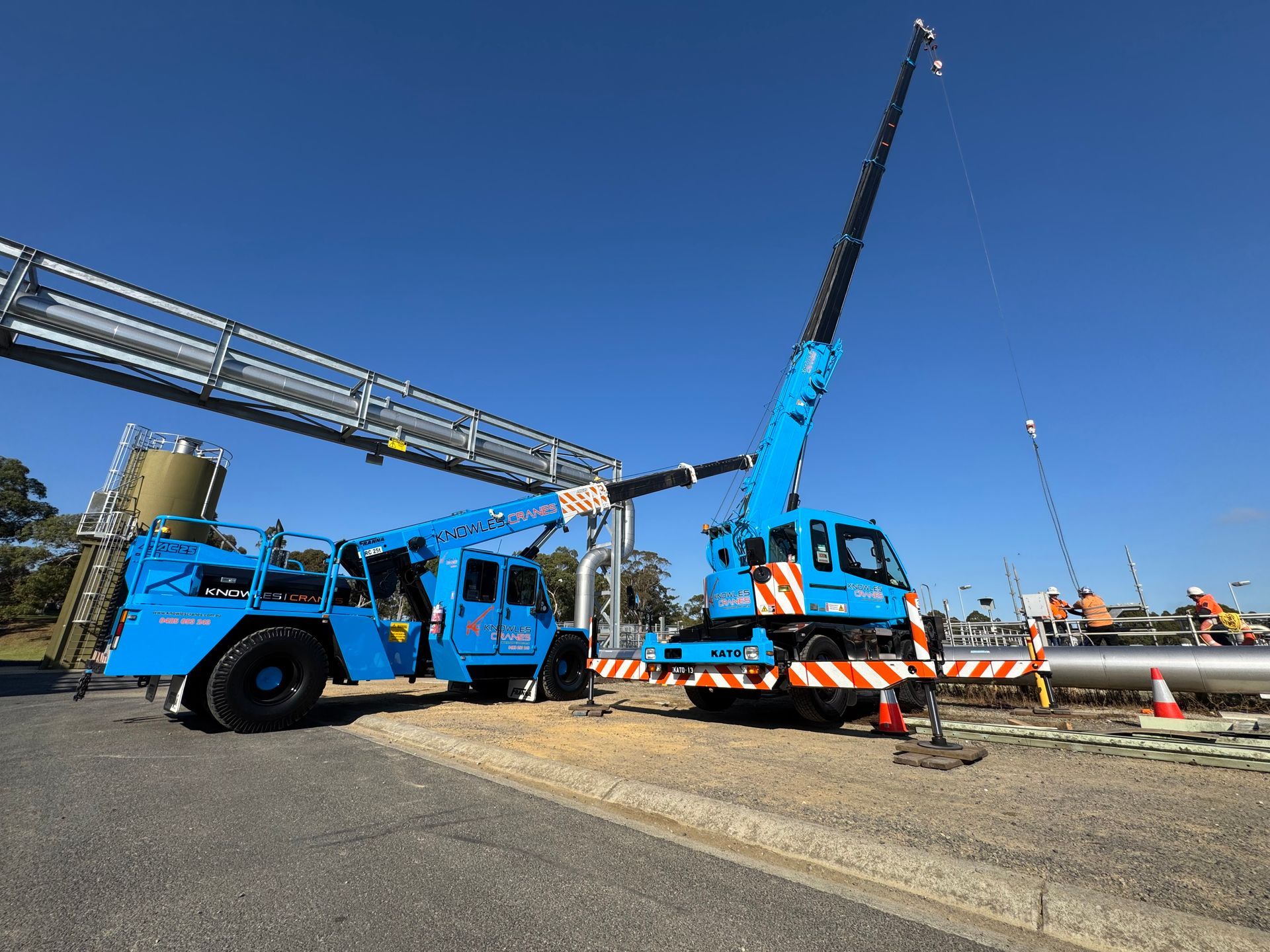 Franna and Kato cranes working together to lift pipework at an industrial site.