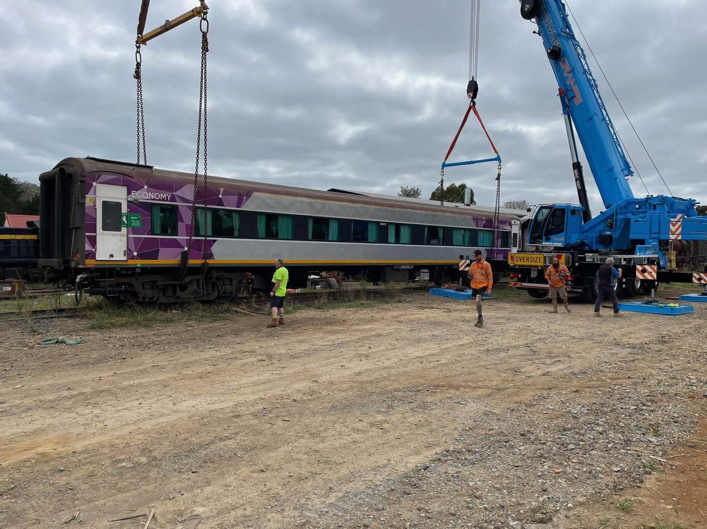Heavy-duty crane lifting a passenger train carriage during a rail relocation project.