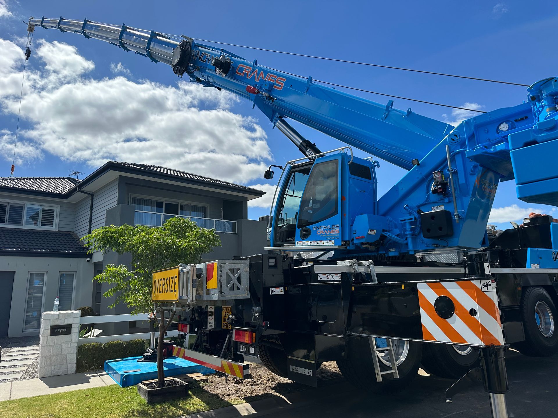 All-terrain crane setup for residential rooftop lifting in a tight suburban street