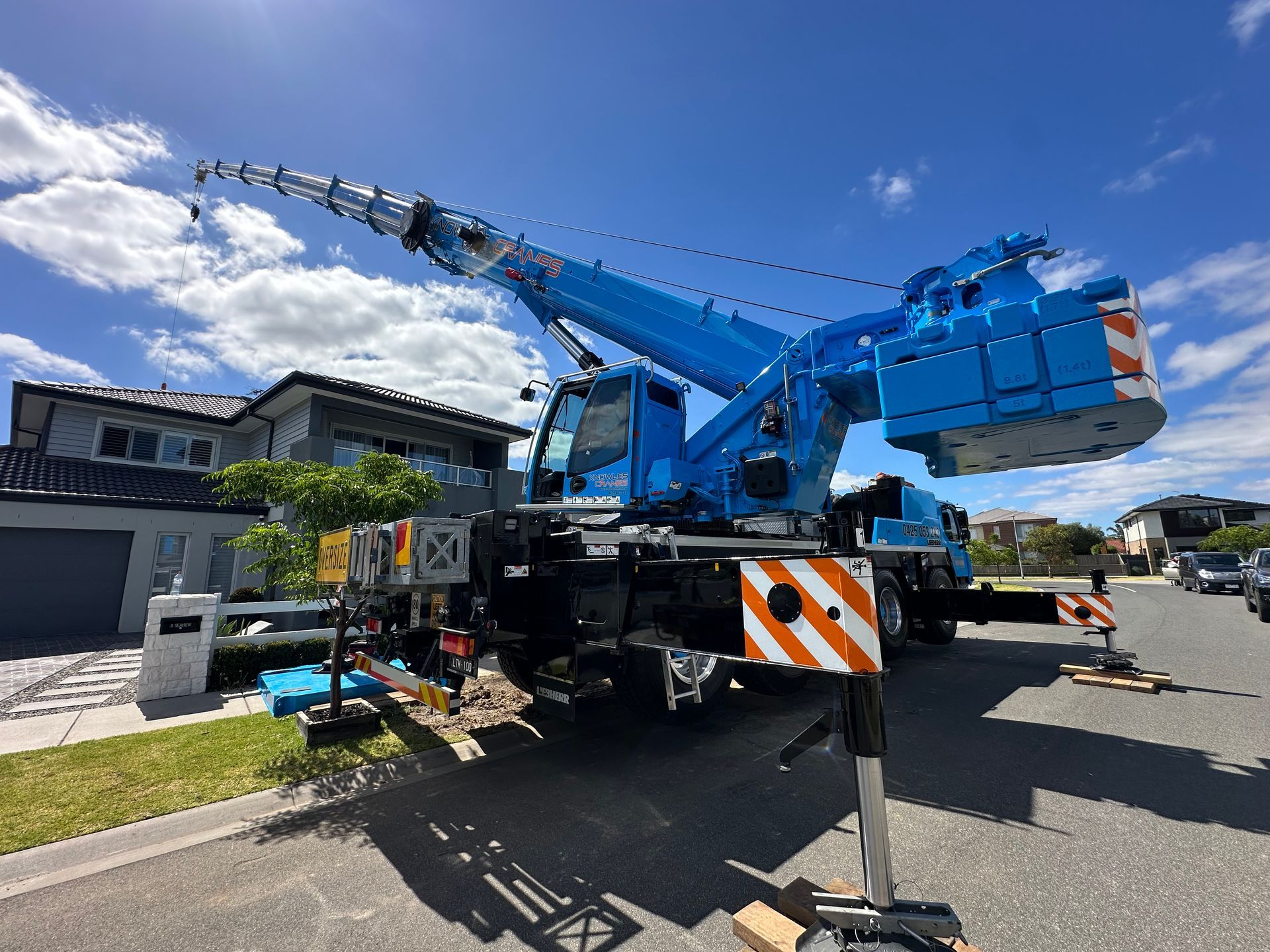 All-terrain crane setup for residential rooftop lifting in a tight suburban street