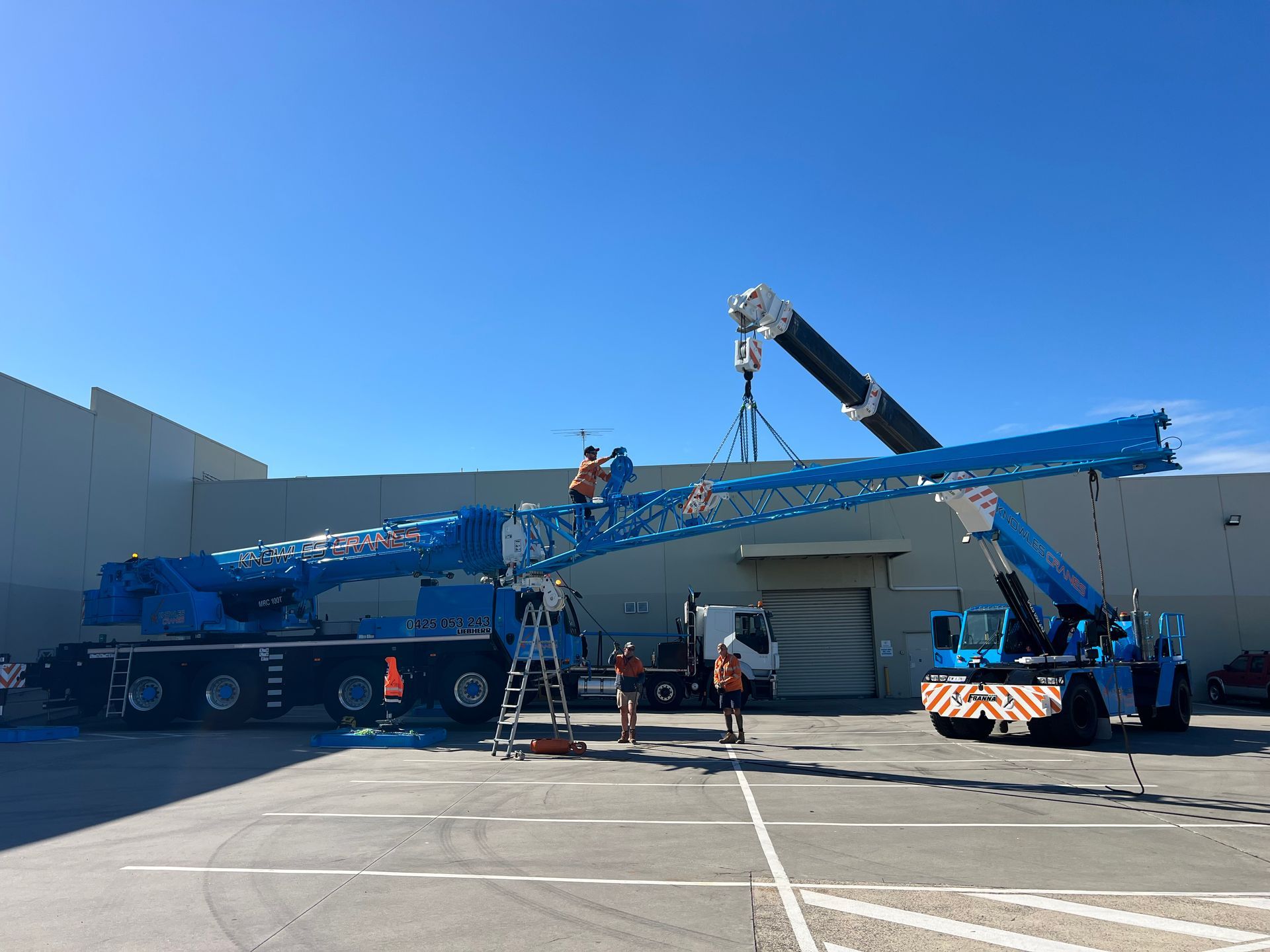 Boom assembly in progress with precision rigging—two cranes align components with care under clear skies.