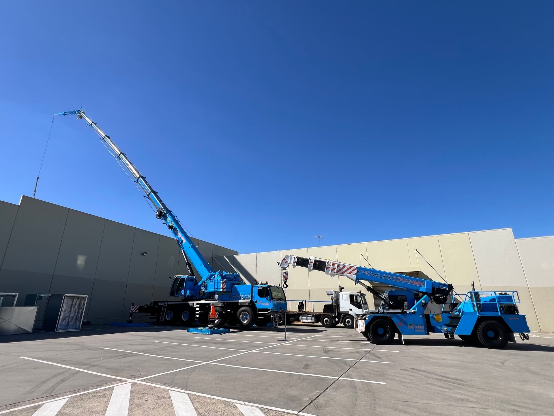 Mobile cranes in action during a rooftop installation—precision lifting over factory walls in a tight-access industrial site.