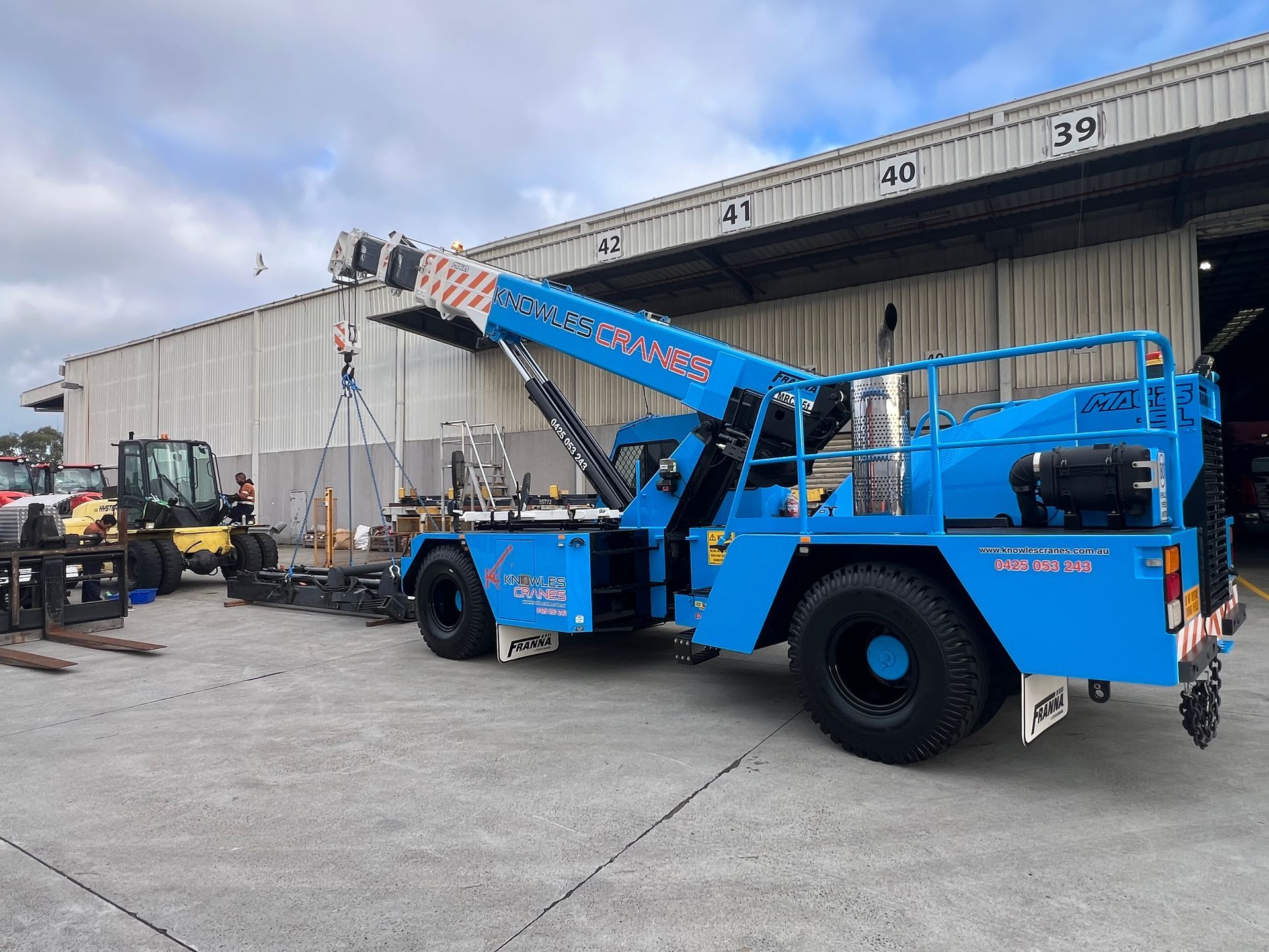 Franna crane lifting machinery outside an industrial warehouse with precision handling