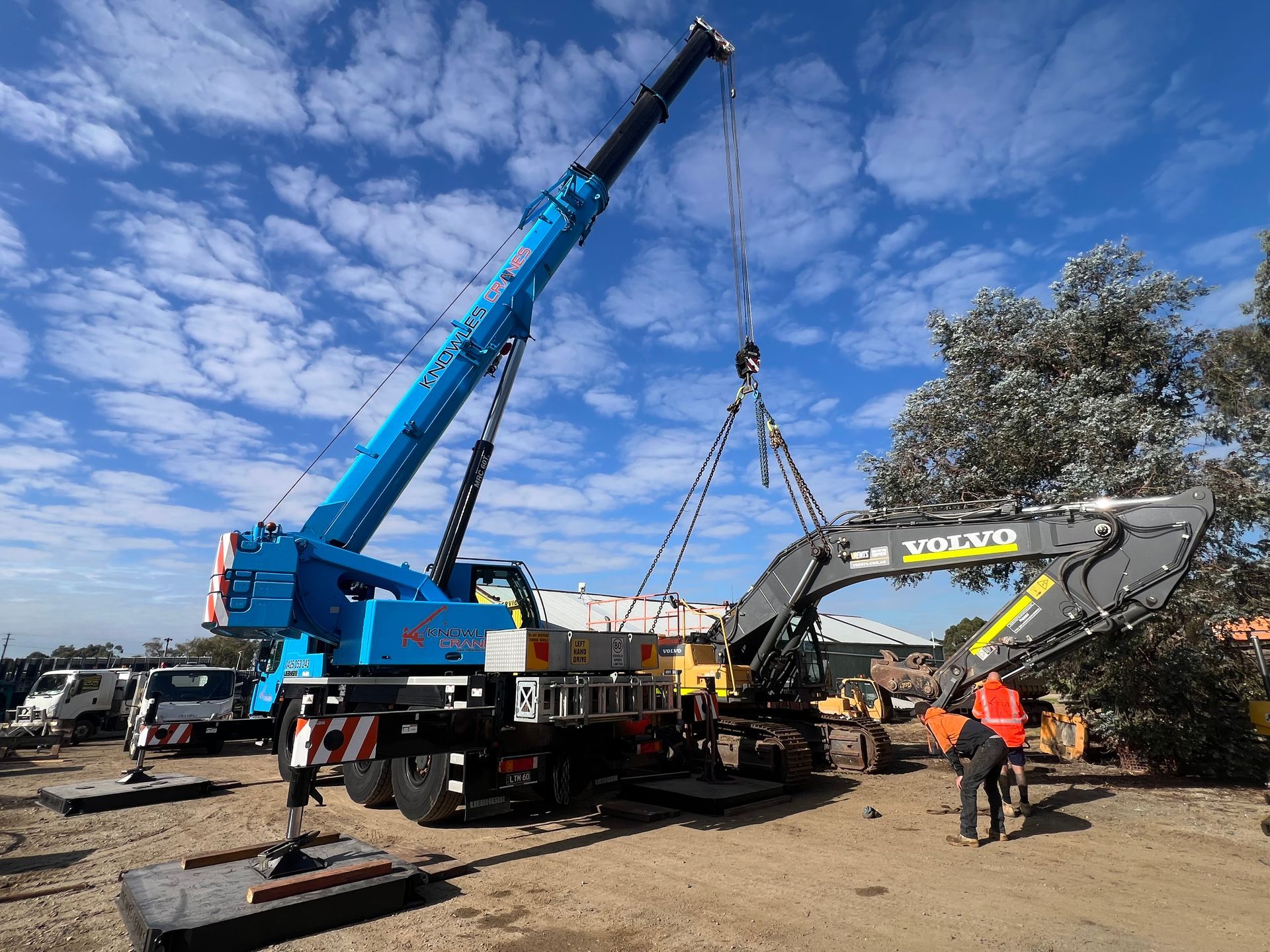 Crane operating at night in a parking lot, lifting a load under bright floodlights.