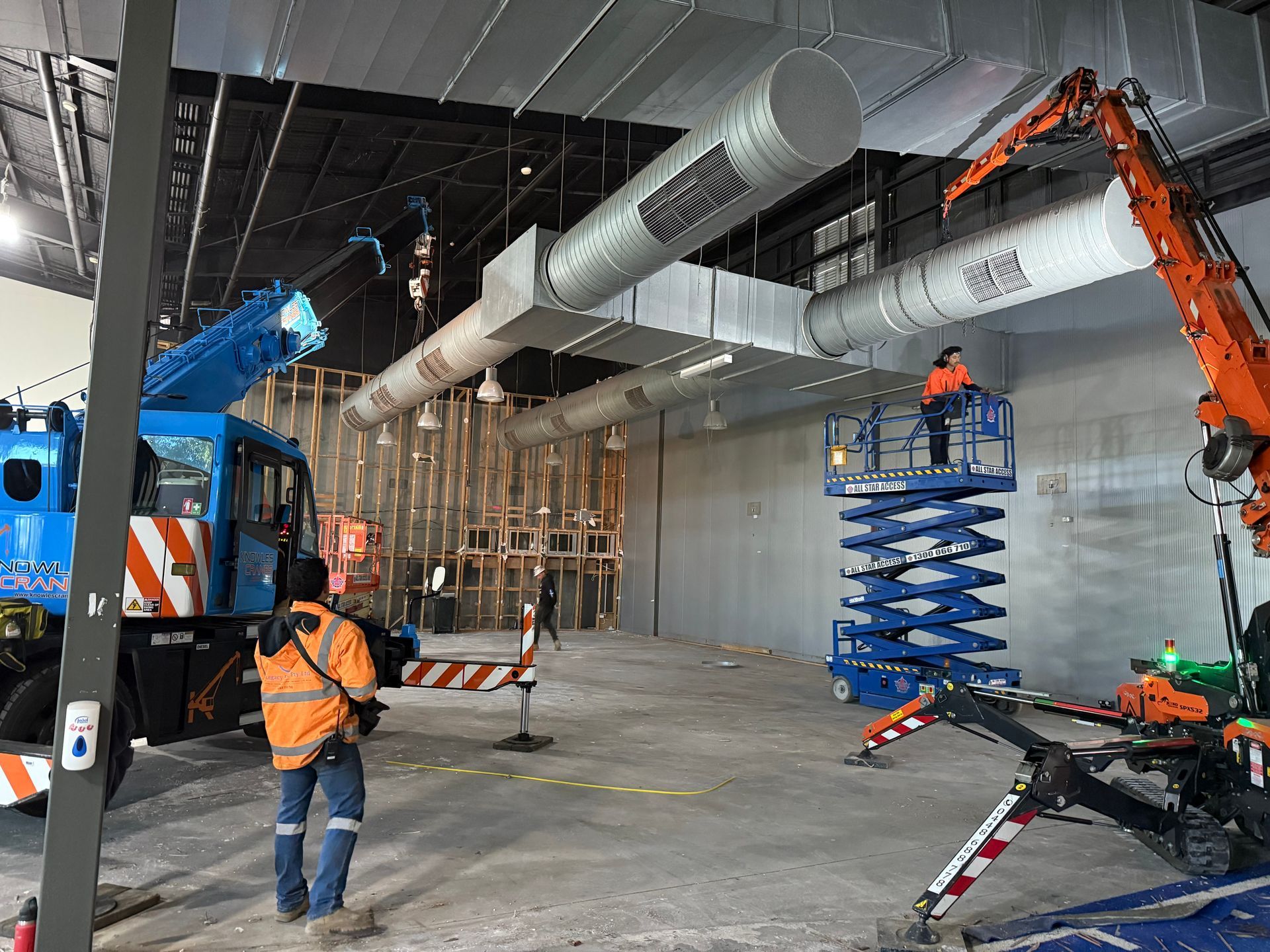 Crane and scissor lift installing large ductwork inside a warehouse