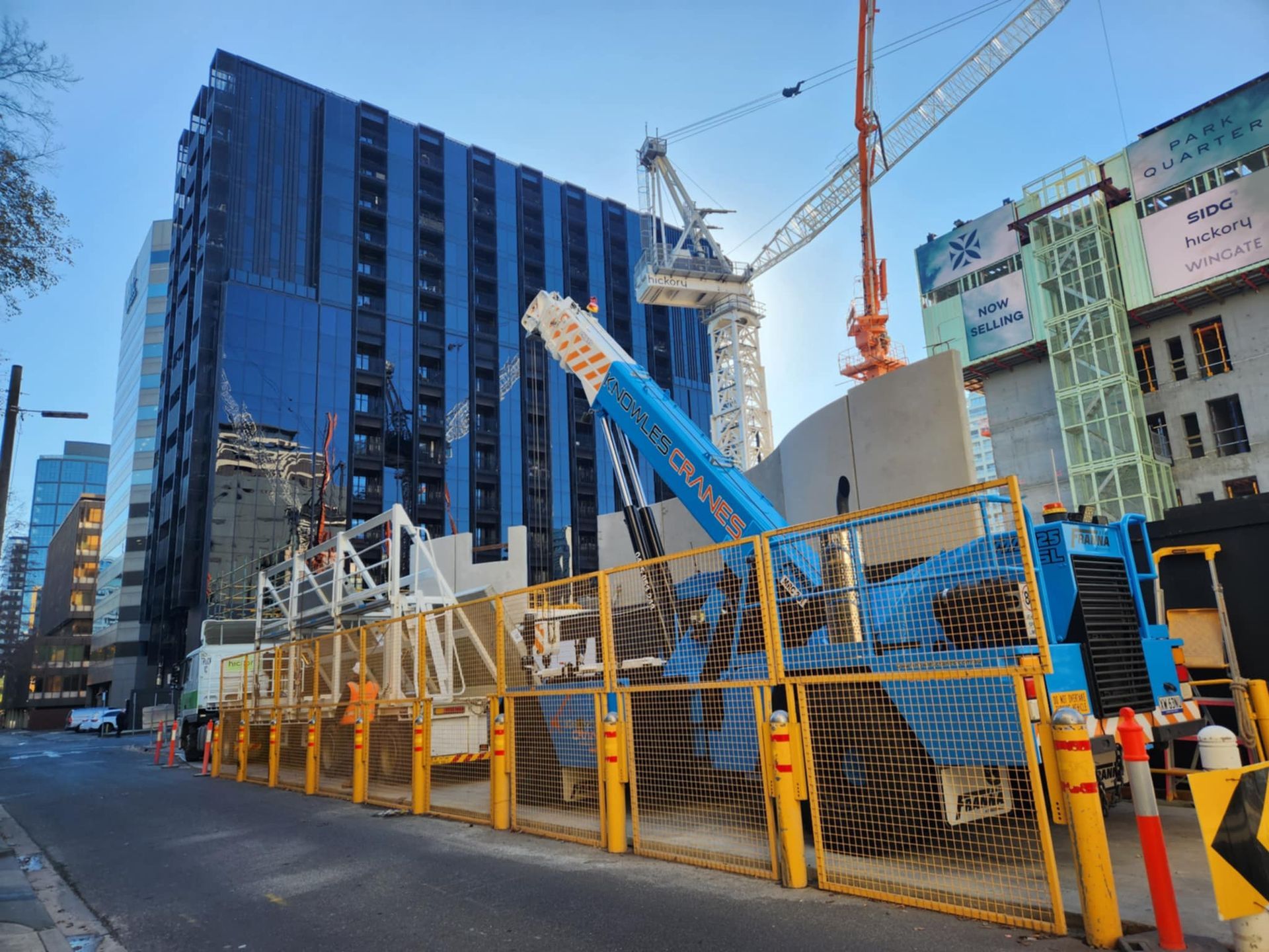 Knowles Cranes Franna crane operating on a city construction site beside high-rise buildings and safety barriers.