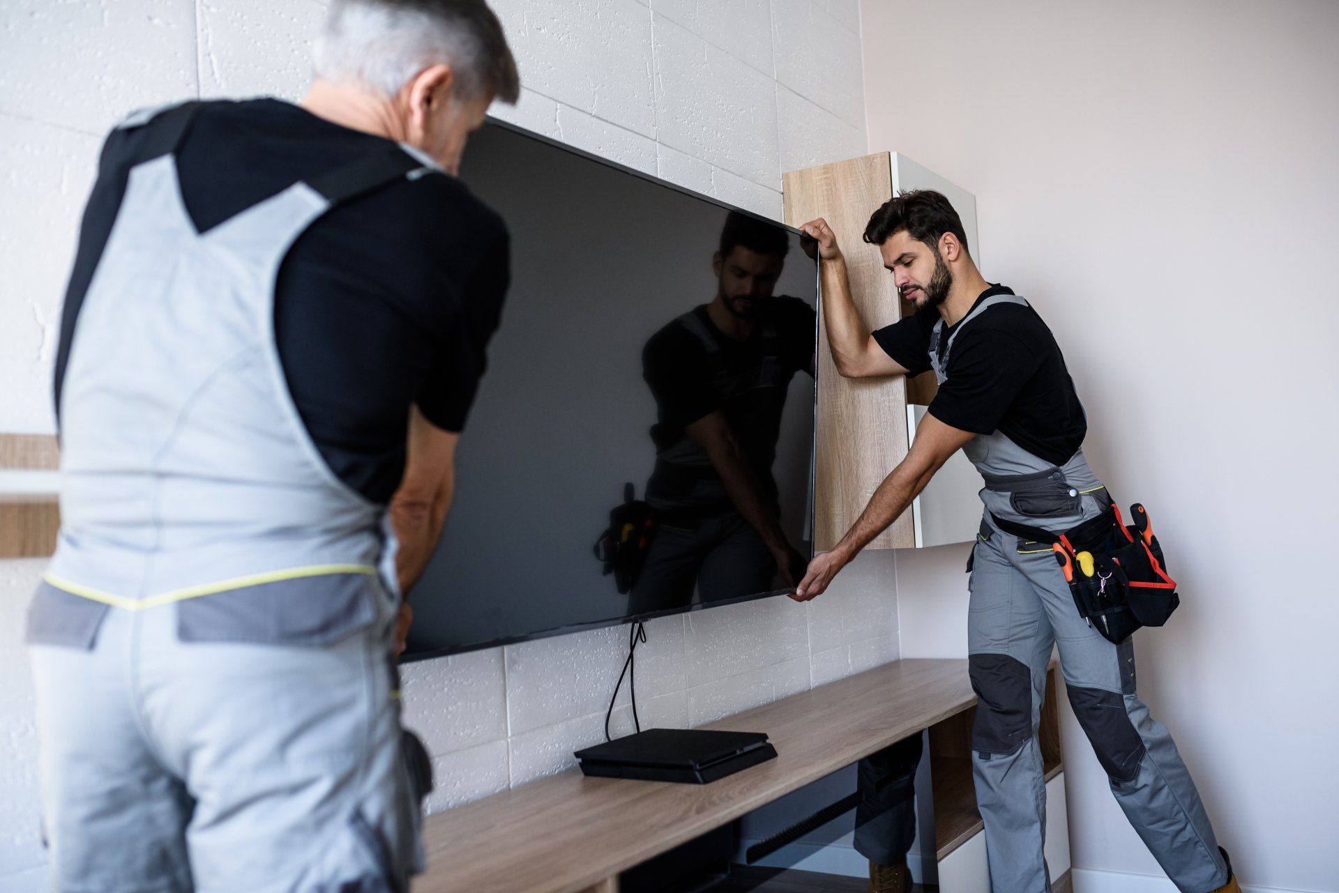 Two professional technicians, workers in uniform installing television on the wall indoors. Construction, maintenance and delivery concept.