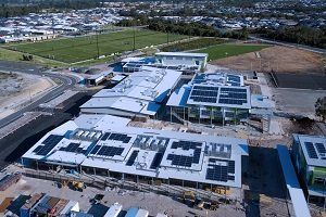 Aerial view of a modern school building with solar panels on the roof and a sports field nearby.