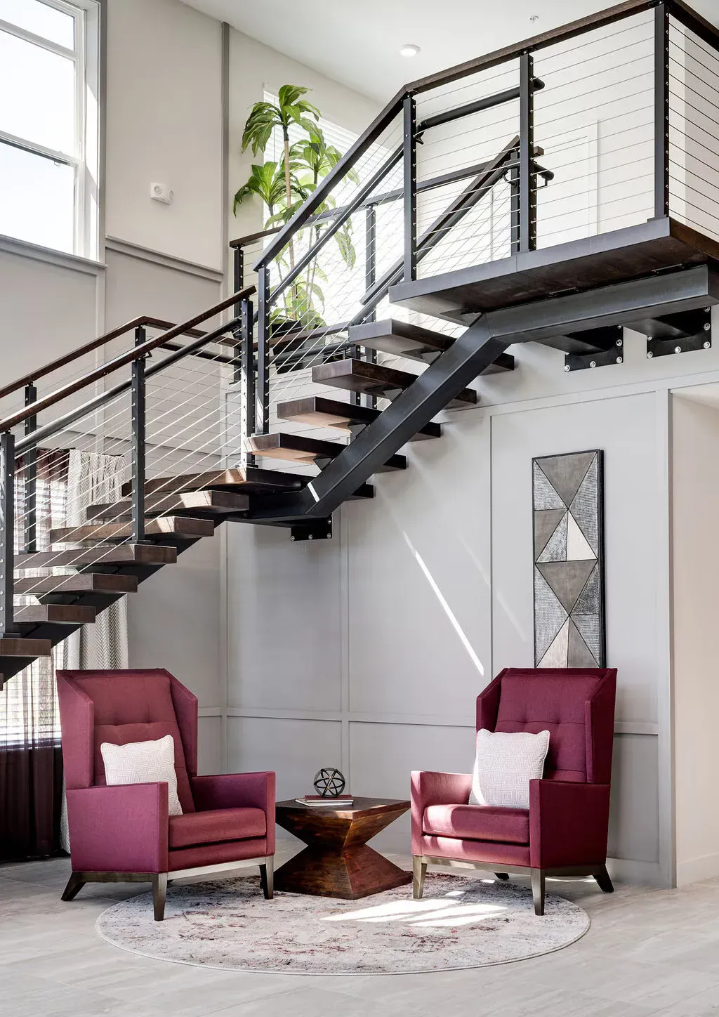 Modern lobby with a metal staircase, burgundy chairs, and a circular rug.