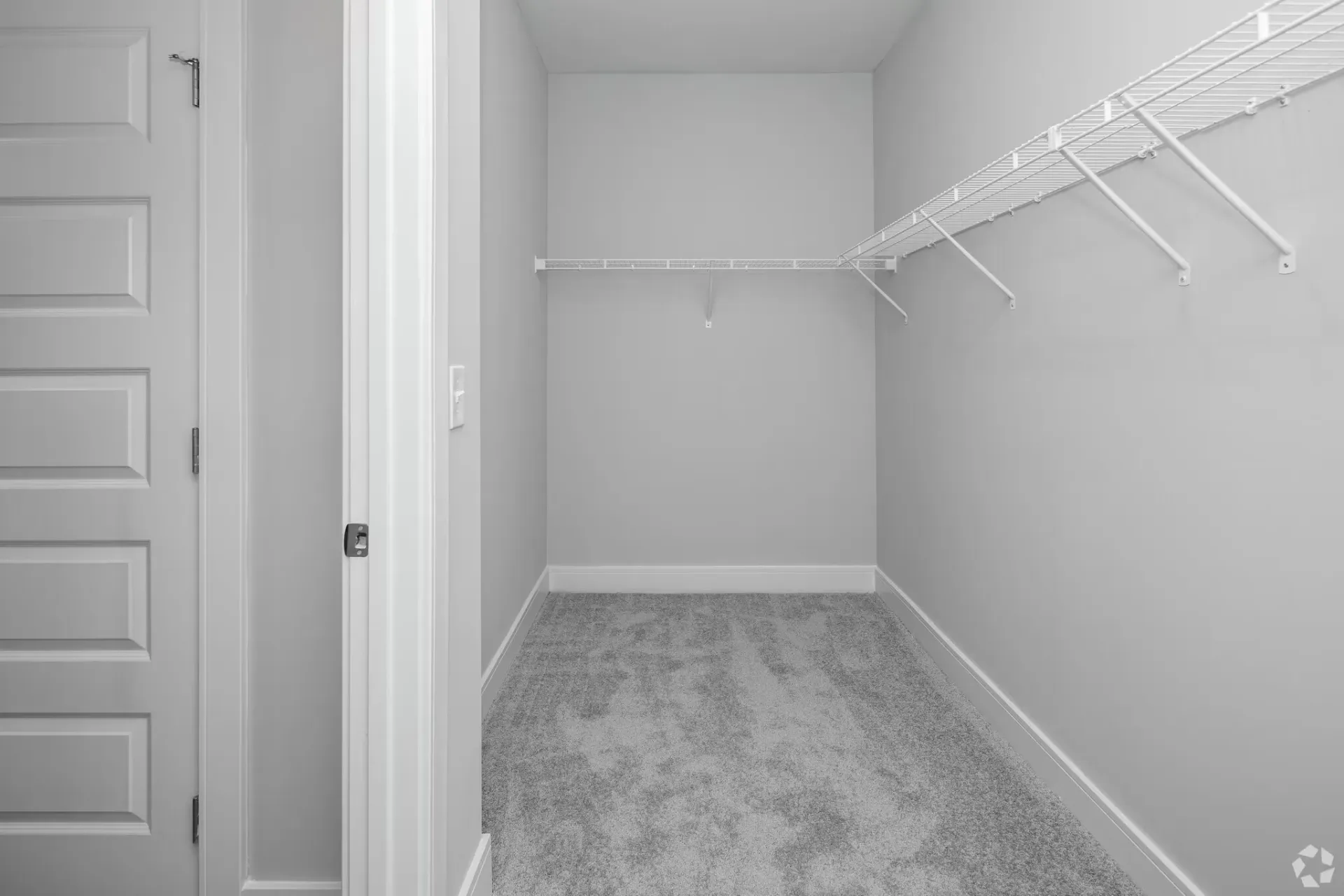 Walk-in closet in a modern apartment with white walls, carpet and wire shelving along the right.