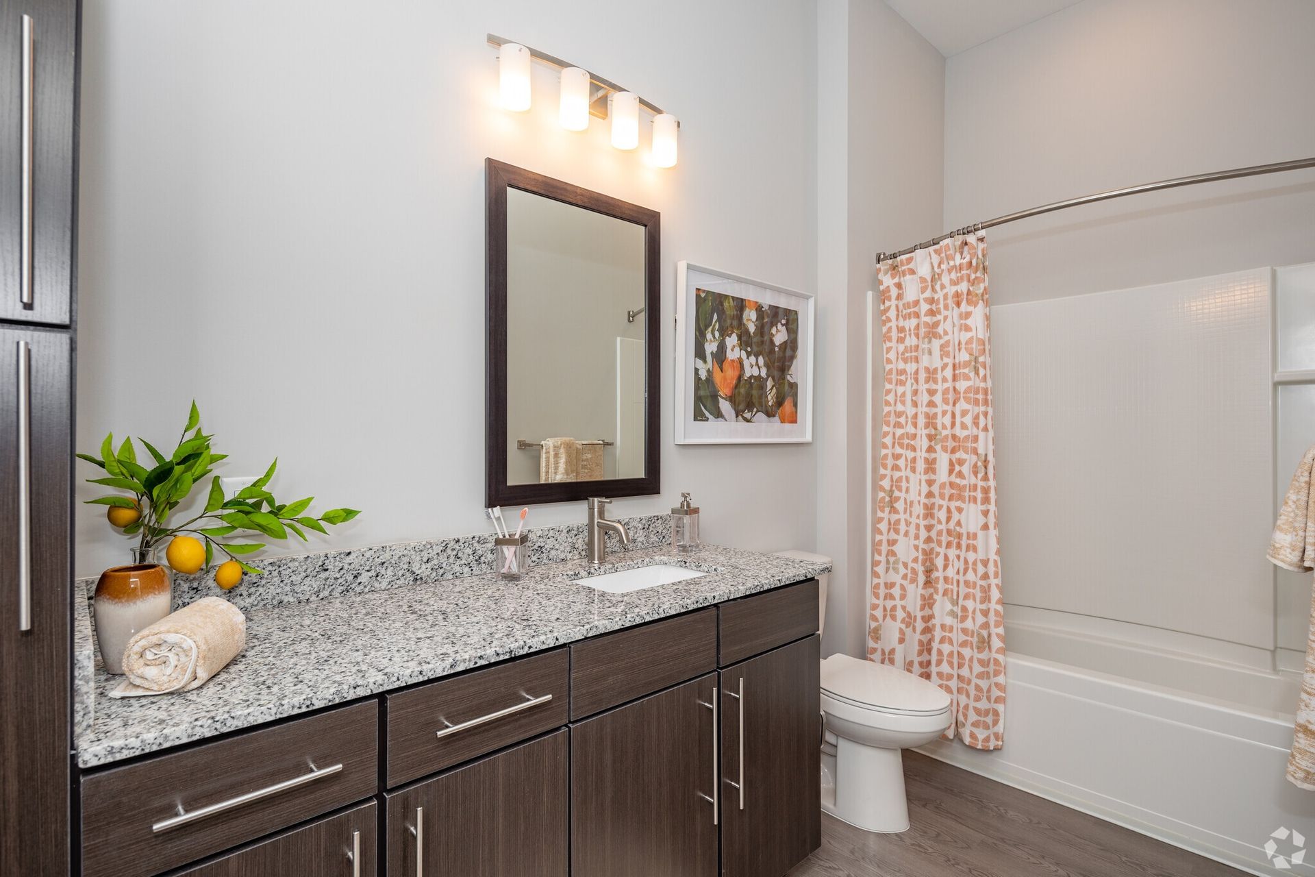 Bathroom with granite countertop, dark wood vanity, mirror, and a shower/tub with peach-pattern curtain.