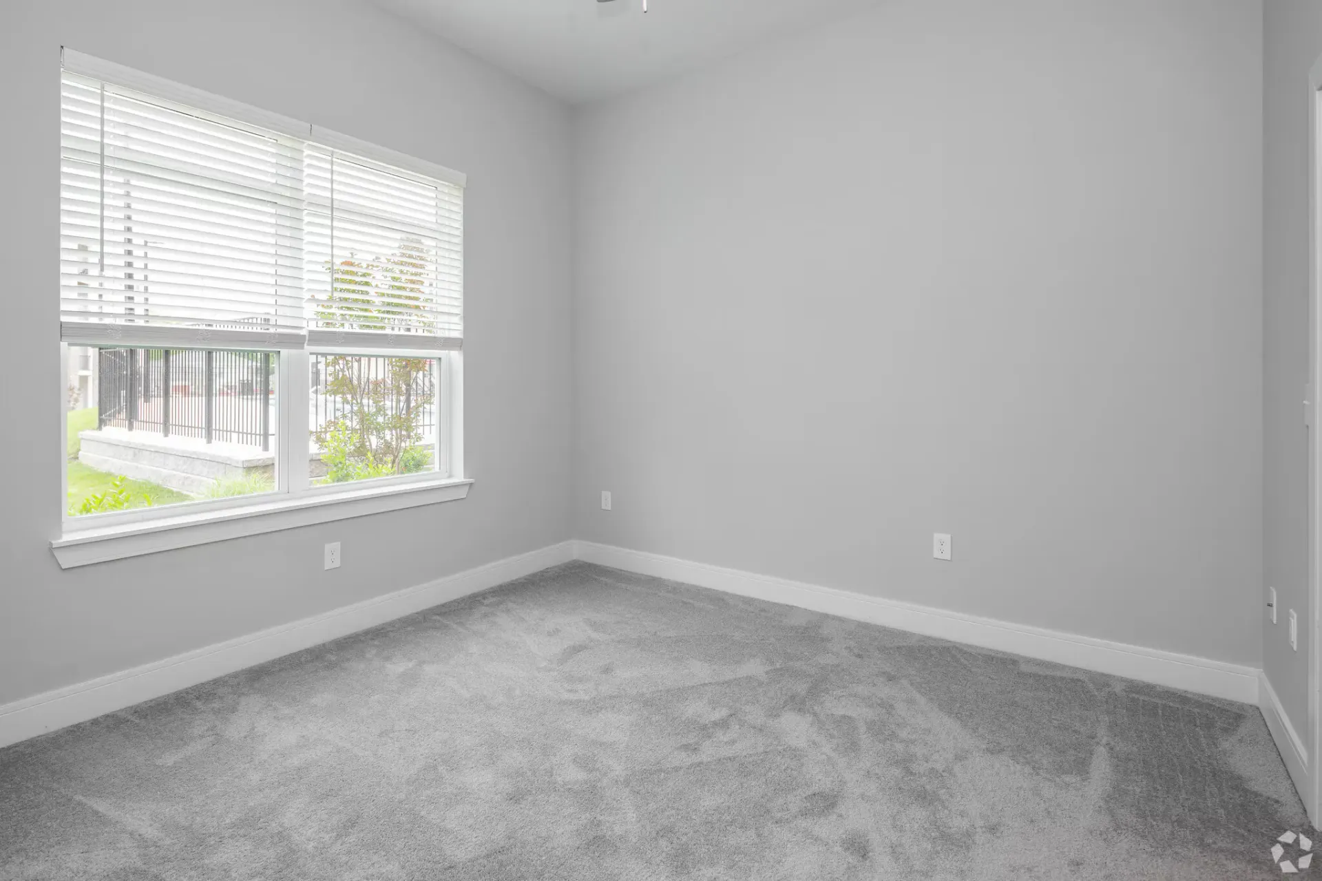 Empty gray bedroom with a large window, white blinds, and carpet.