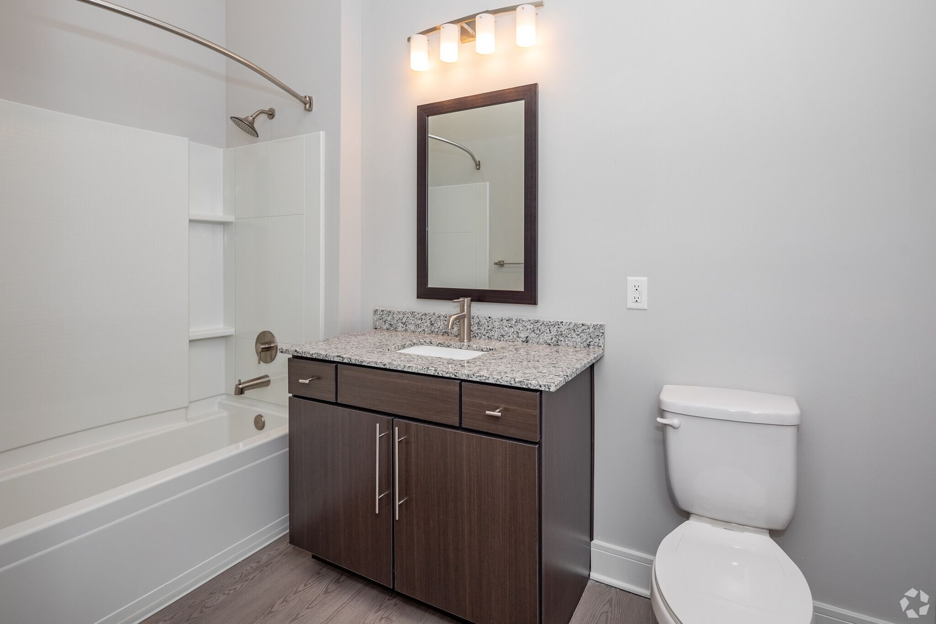 Modern bathroom with granite countertop vanity, mirror, shower-tub, and toilet.