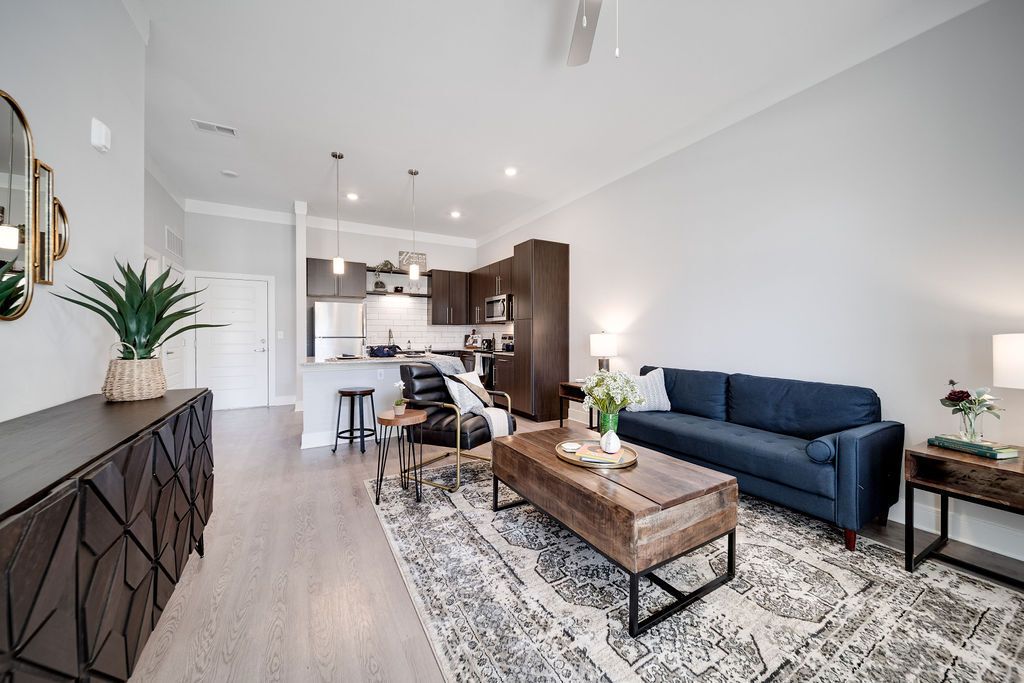 Open-concept living area with kitchen in a modern apartment, featuring a blue sofa and wooden coffee table.