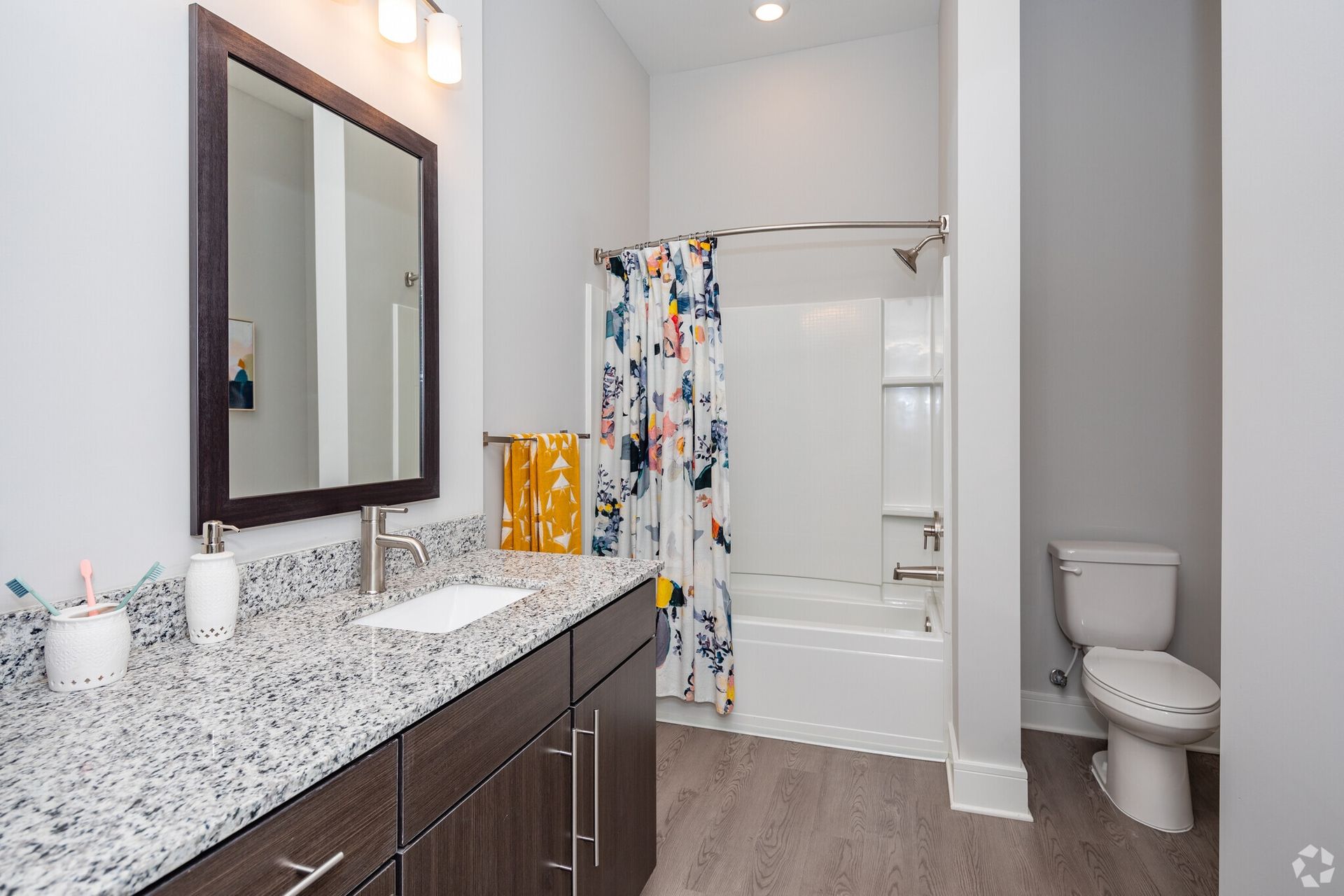 Bathroom with granite vanity, framed mirror, single sink, shower-tub, and toilet.