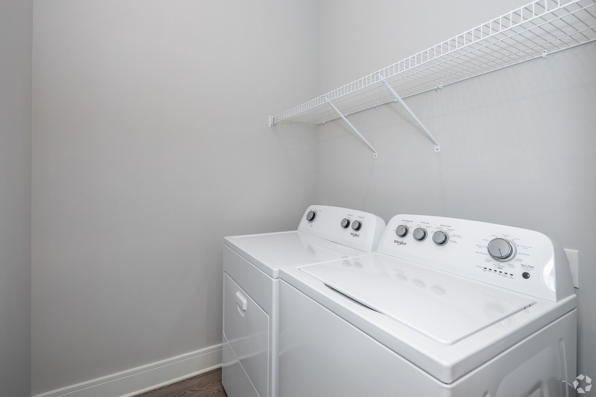 White laundry room with a side-by-side washer and dryer and a white wire shelf above.