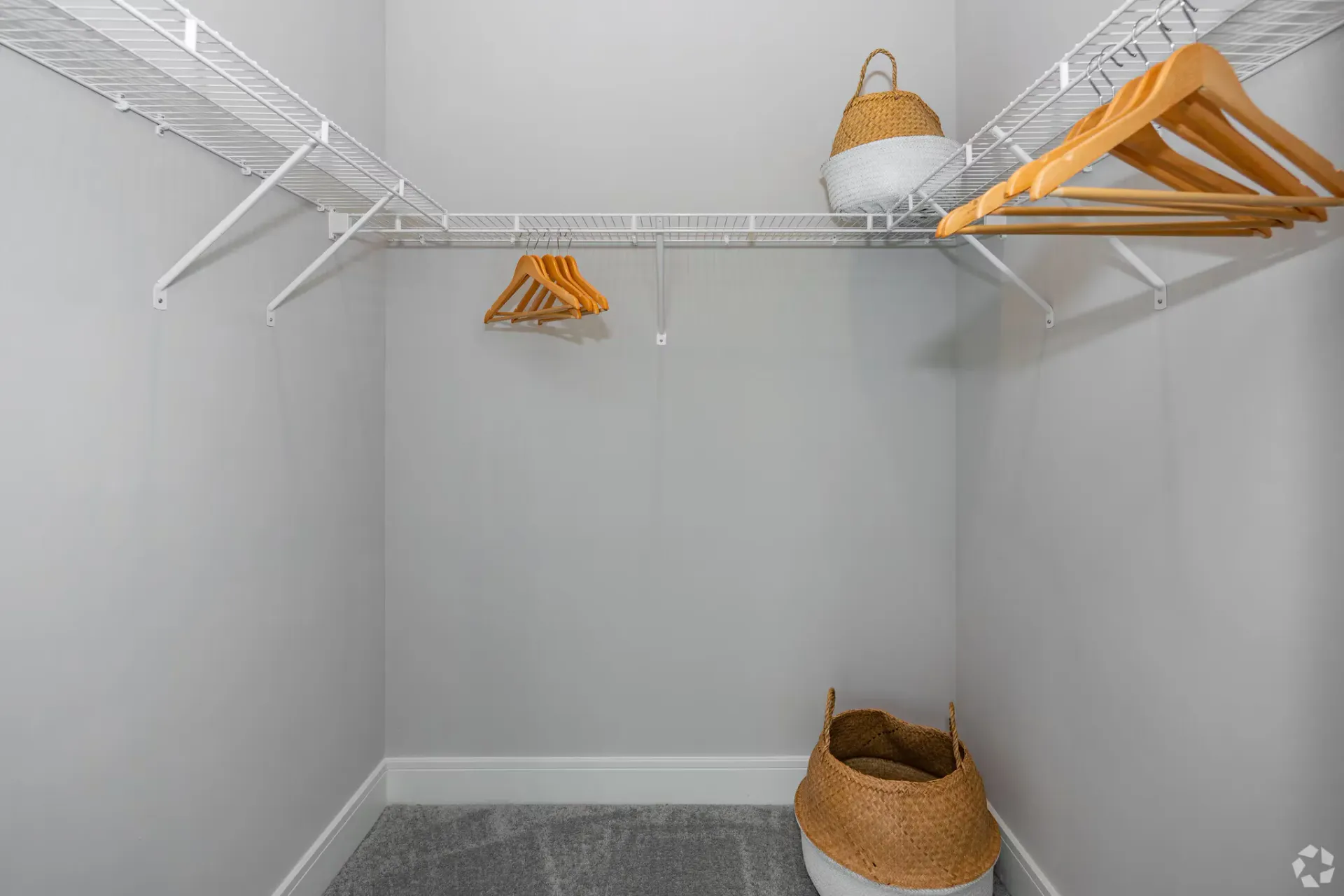 Walk-in closet with white wire shelves, wooden hangers, and a woven basket.