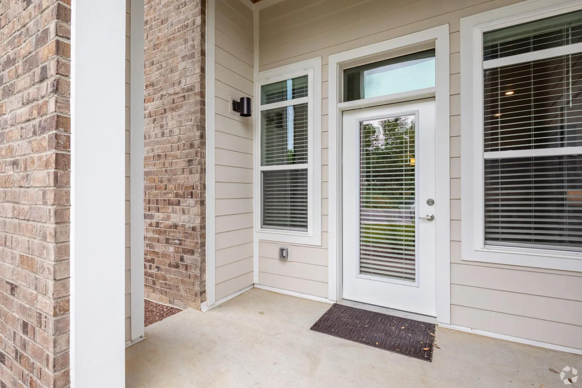 Exterior entry door of an apartment with a window and beige siding beside brick.