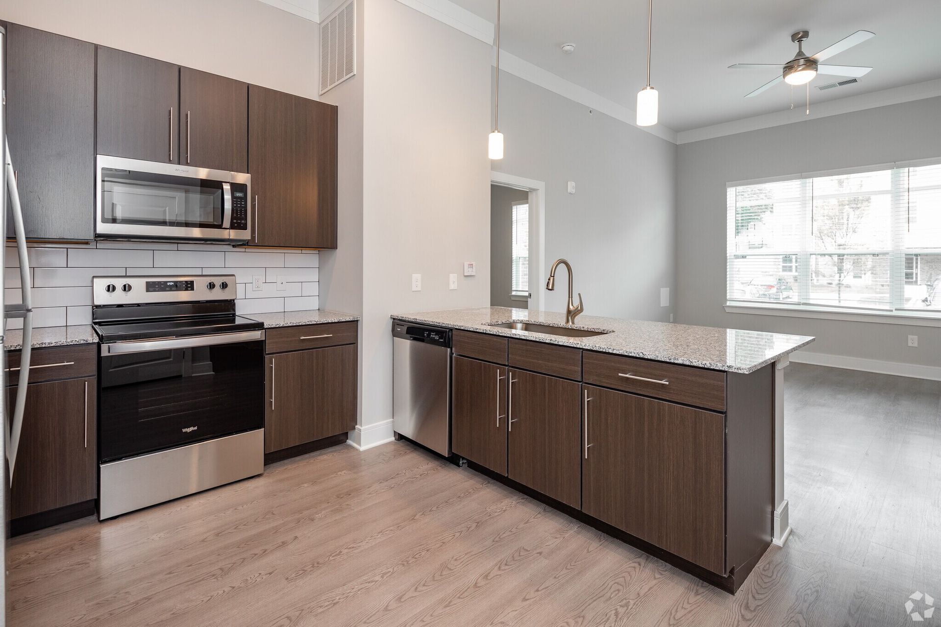 Open-concept kitchen with dark wood cabinets, stainless steel appliances, granite island, and large window.