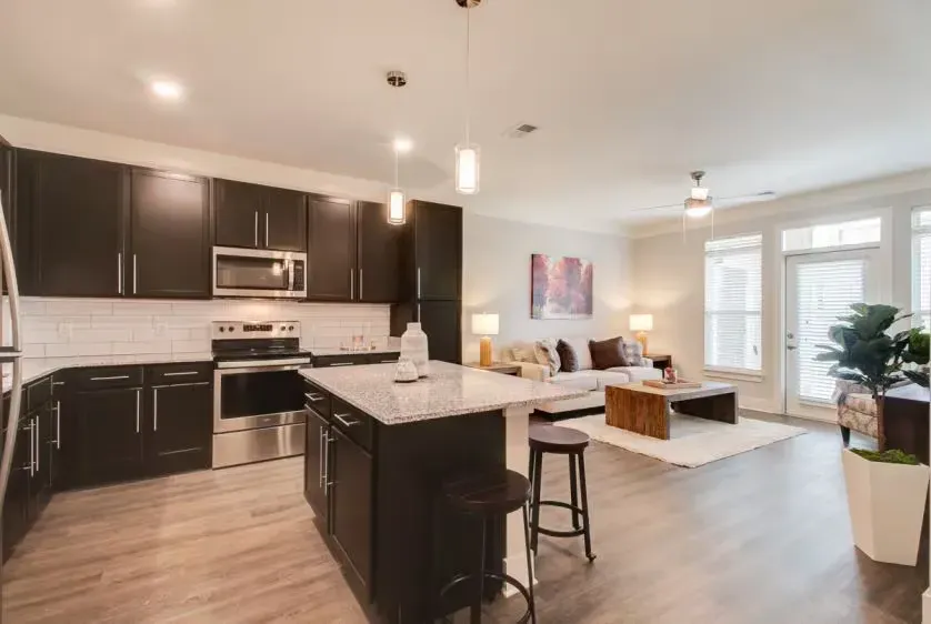 Open-concept kitchen and living area in a modern apartment with dark cabinets and island.