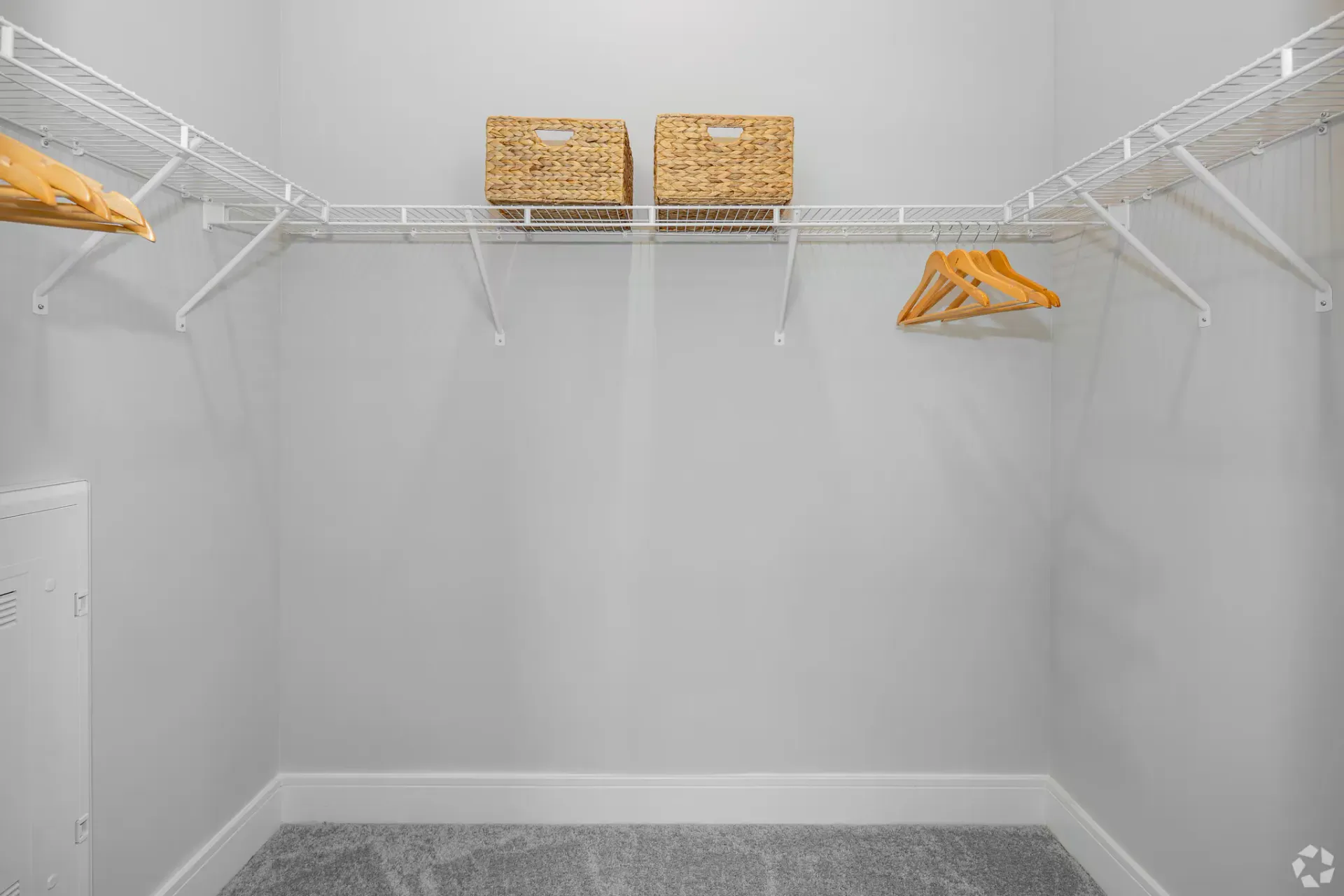 Walk-in closet with white wire shelves, wooden hangers, and woven baskets.