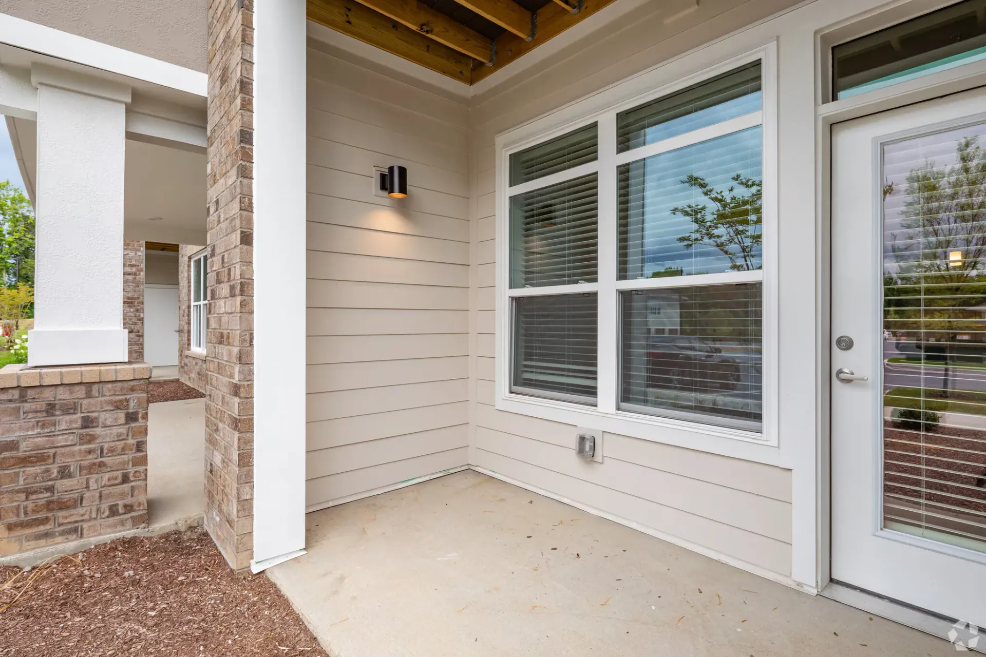 Exterior corner of an apartment building showing siding, brick column, and a glass door.