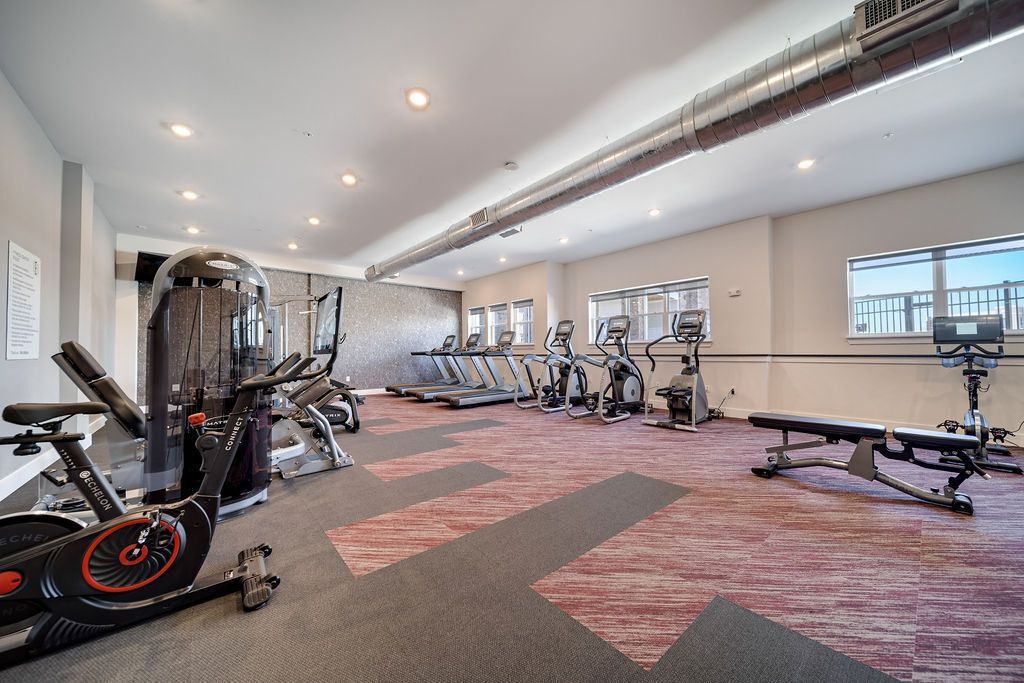 Bright apartment gym with treadmills, stationary bikes, and a weight bench.