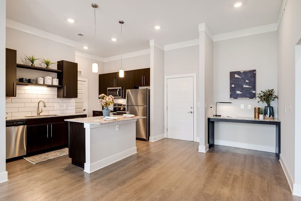 Open-concept kitchen with island, dark wood cabinets, stainless steel appliances, and a white tile backsplash.
