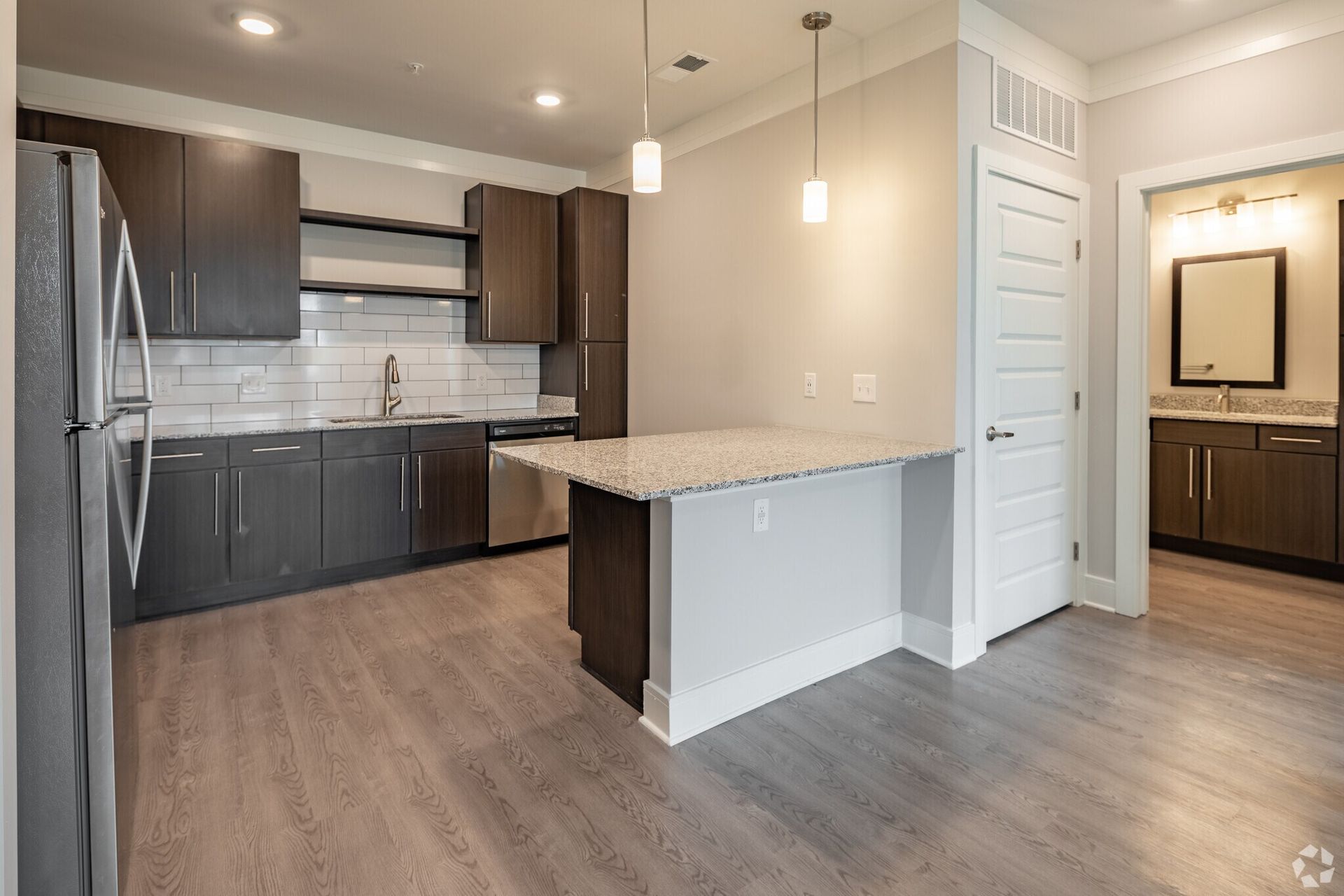 Modern apartment kitchen with dark cabinets, stainless appliances, and a granite island.