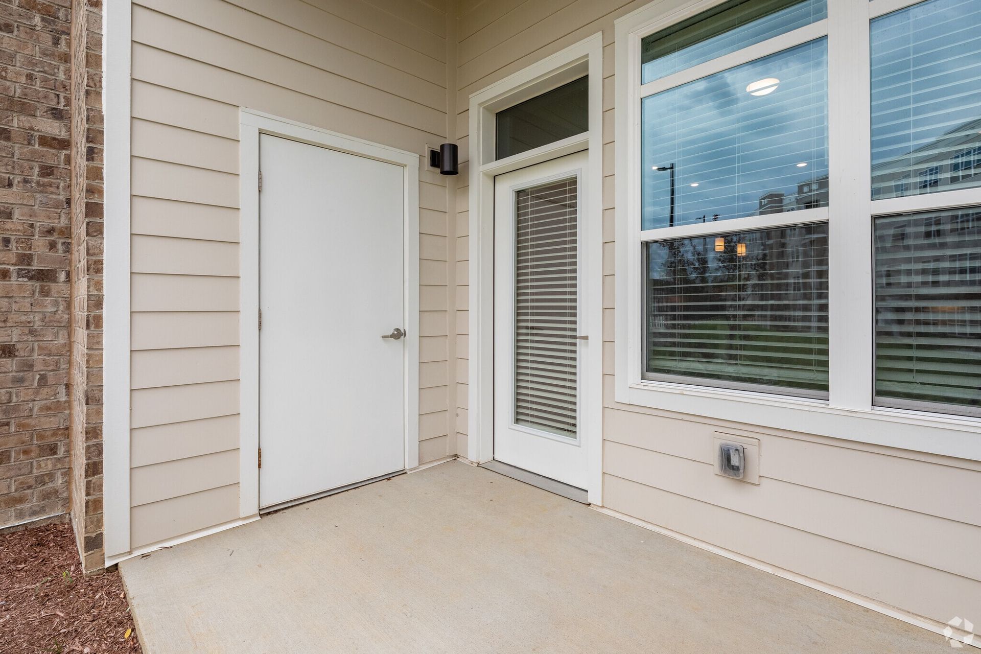 Exterior entry to a beige apartment with a white door and large window with blinds.