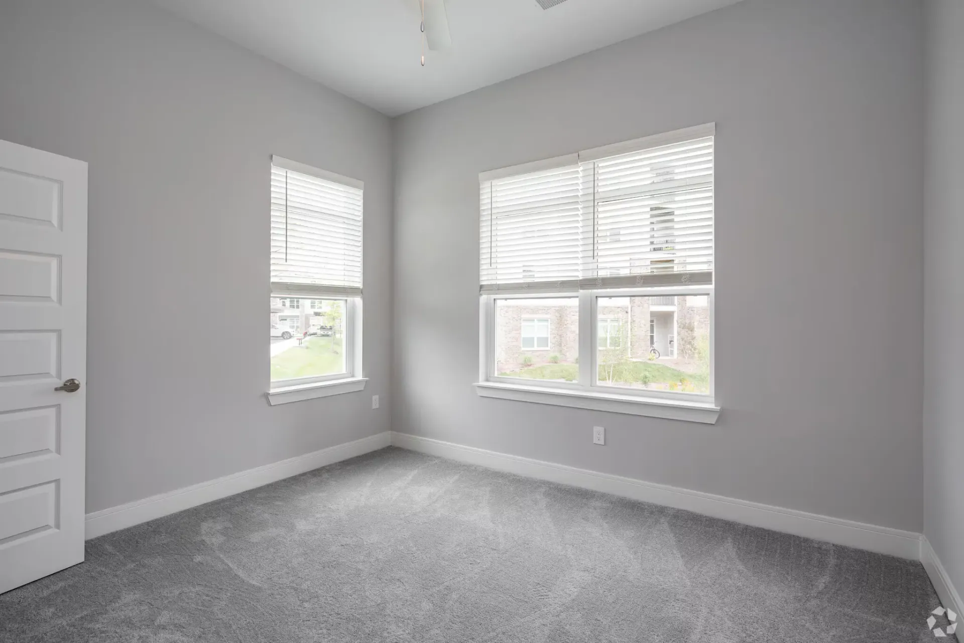Empty bedroom with gray walls, two windows with white blinds, and carpet.