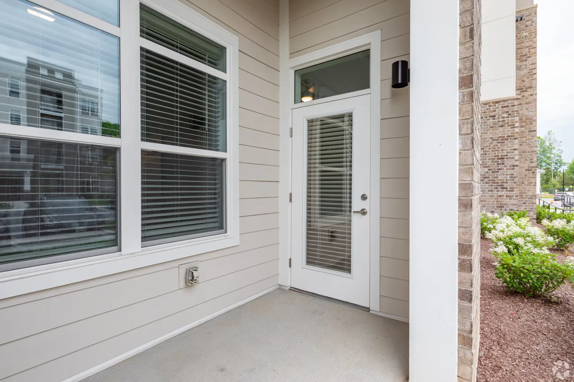 Ground-level apartment entry door with glass panel and blinds beside a window.