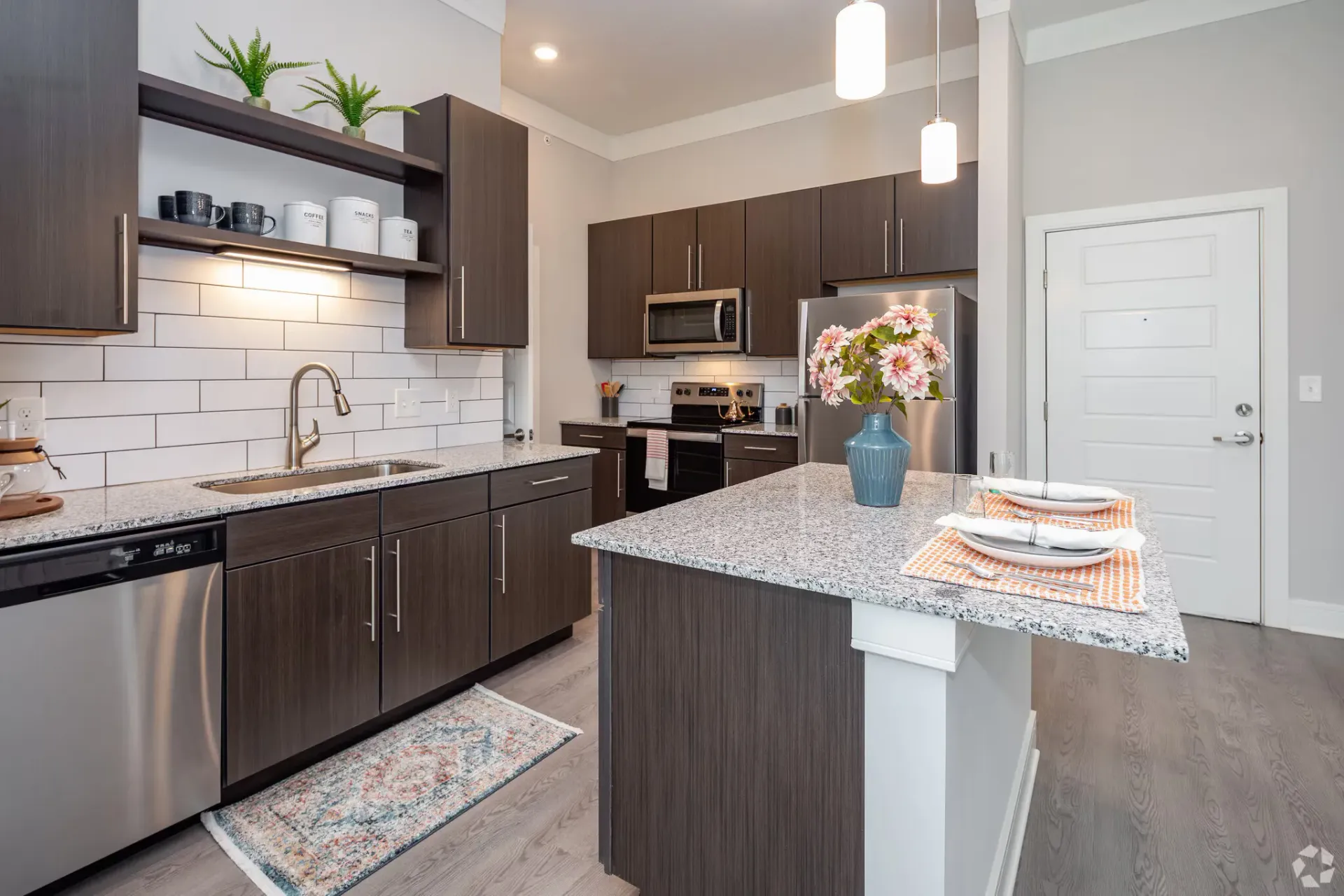 Modern apartment kitchen with granite counters, dark wood cabinets, and stainless appliances.