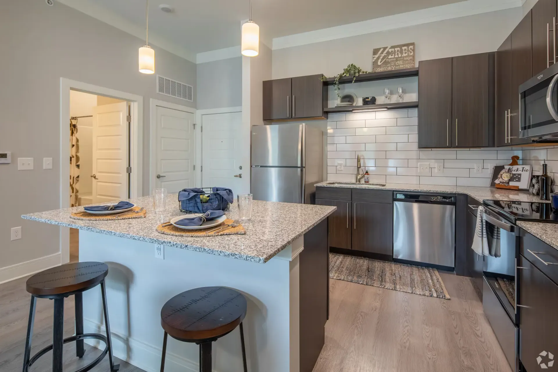 Modern apartment kitchen with granite island, stainless-steel appliances, and dark wood cabinets.