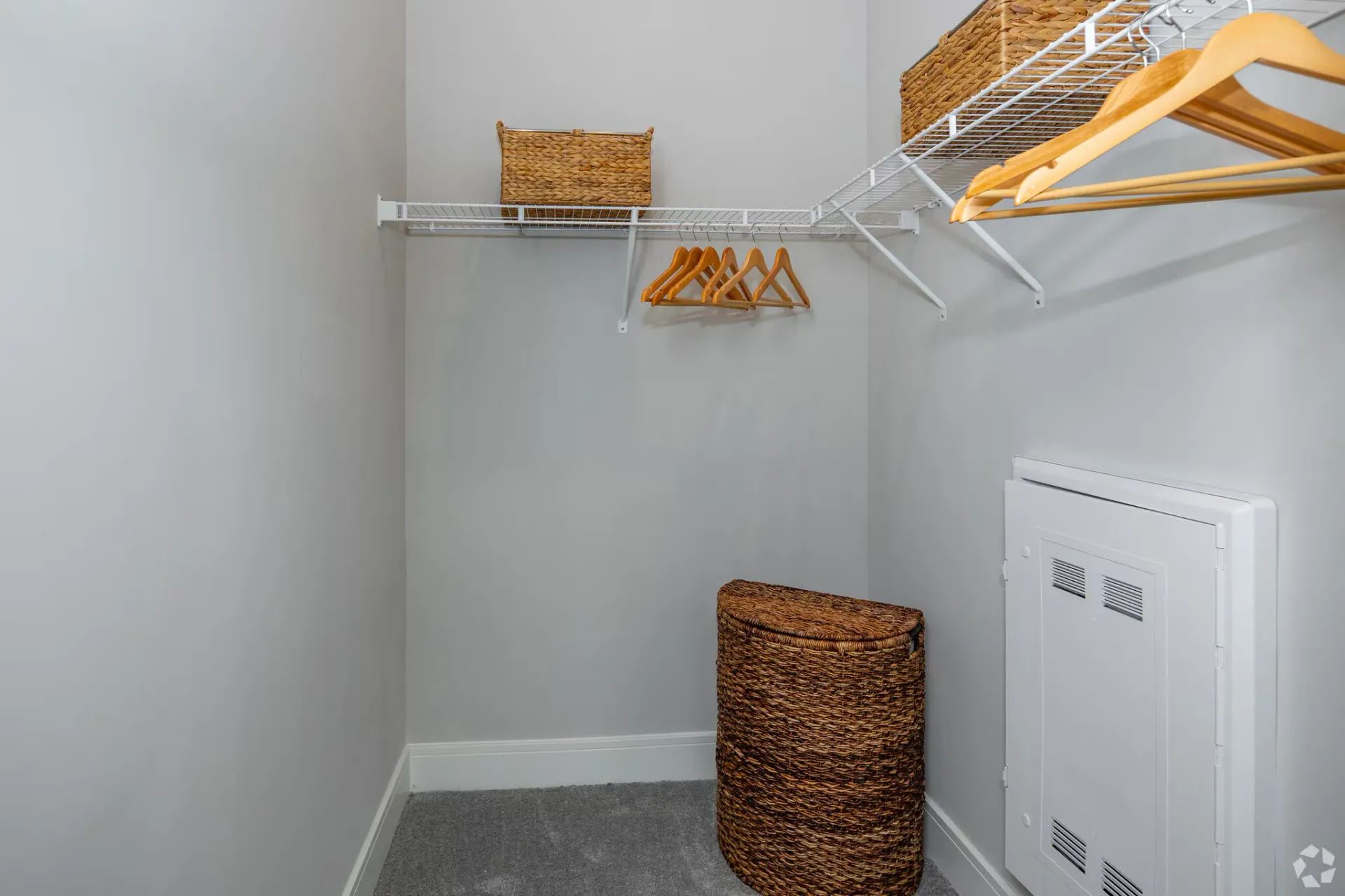 Walk-in closet with white wire shelving, wooden hangers, and wicker storage baskets.