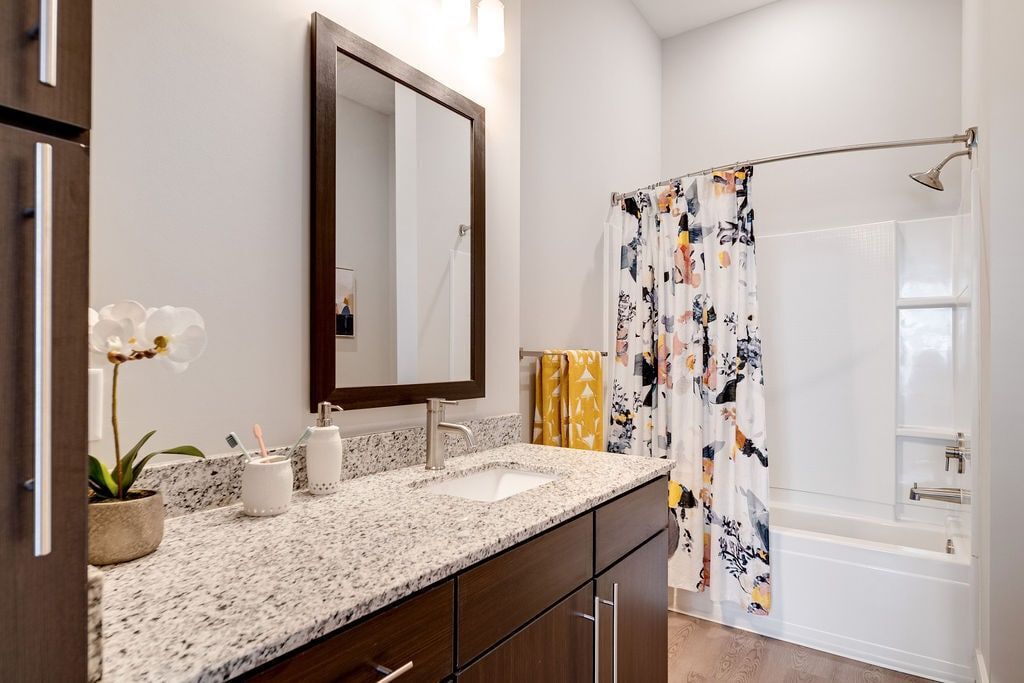 Bathroom featuring a granite countertop, single sink, dark wood vanity, large mirror, and a floral-pattern shower curtain.
