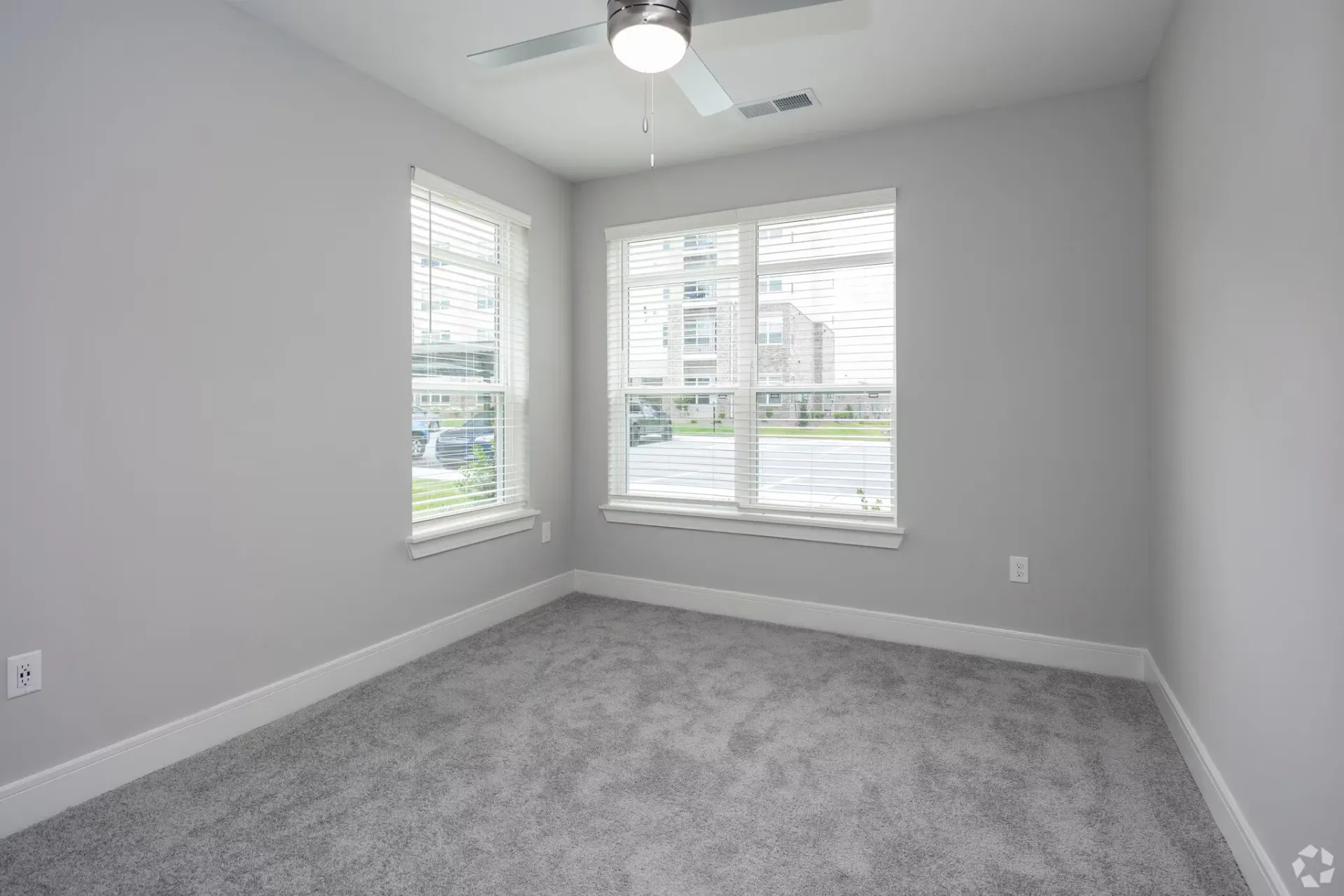 Empty gray-carpeted bedroom with two windows and a ceiling fan.