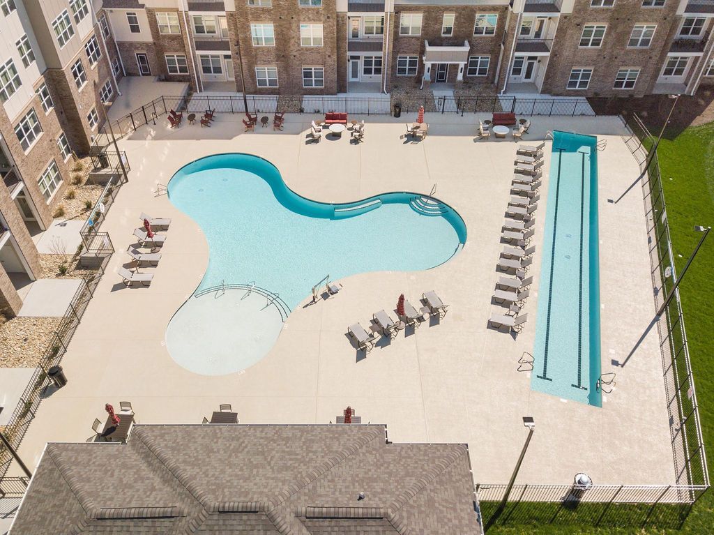 Aerial view of a curved pool and a long rectangular lap pool surrounded by apartment buildings.