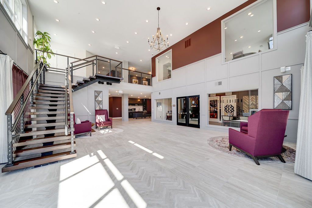 Spacious lobby with stairs, seating, and high ceilings. Burgundy accents on walls and furniture.
